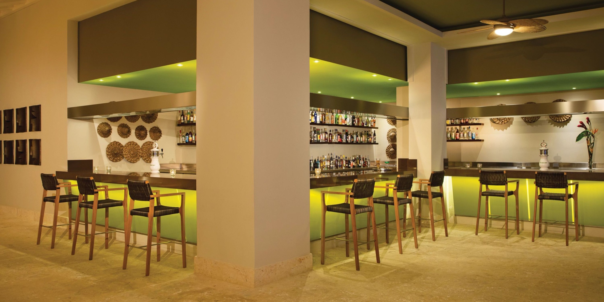 The Dreams Onyx features a contemporary design with two counters, ambient green lighting, high chairs, and an assortment of bottles showcased on shelves. The walls are adorned with circular woven patterns.
