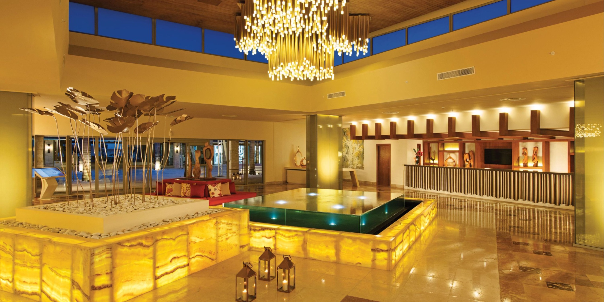 Dreams Onyx offers a luxurious atmosphere featuring a large chandelier, modern art pieces, an illuminated water feature, and a comfortable seating area in its hotel lobby.