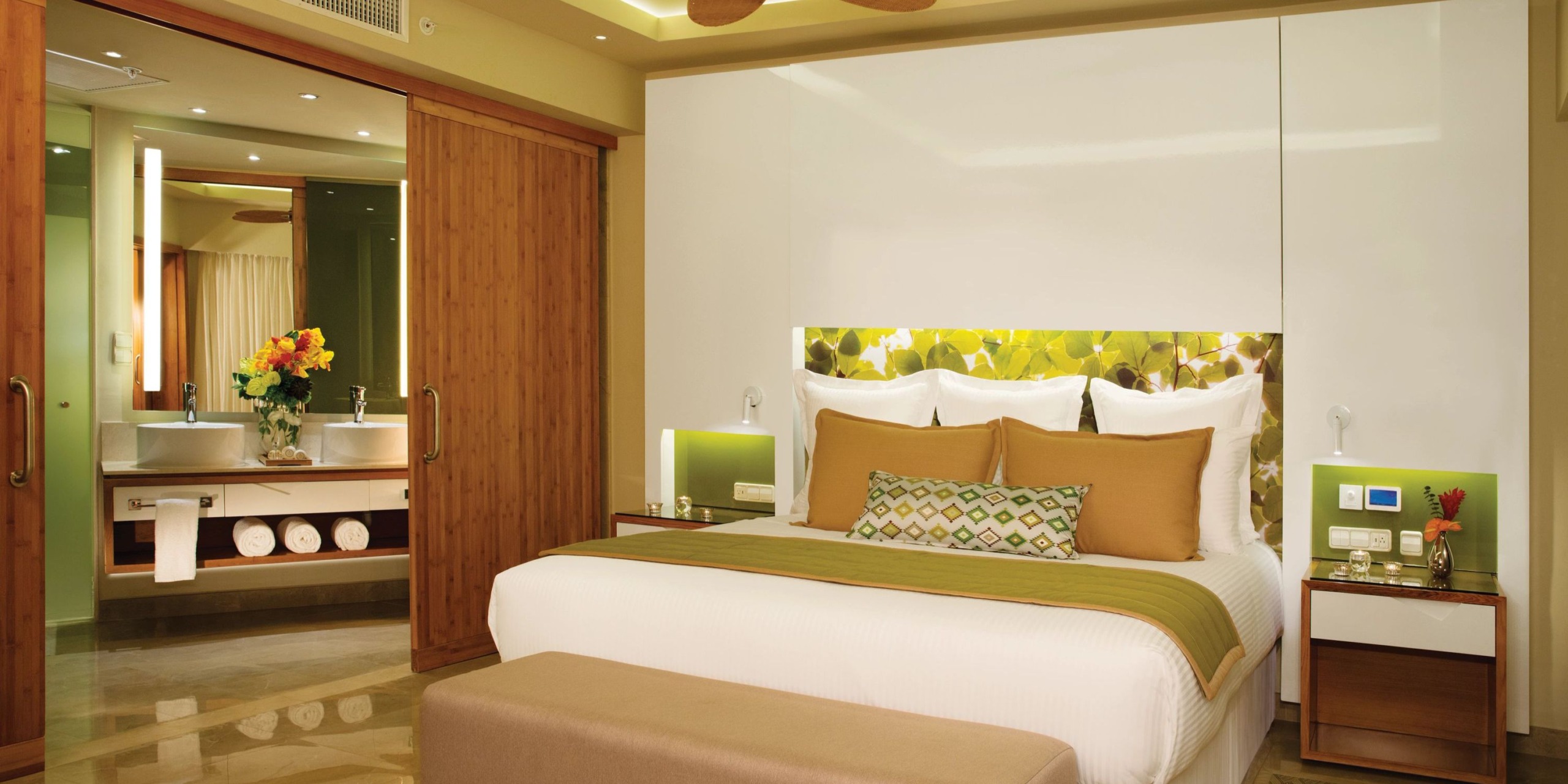 Dreams Onyx hotel room featuring a double bed, adorned with green and brown accents, includes a sliding door that opens to a brightly lit bathroom equipped with a sink and large mirror.