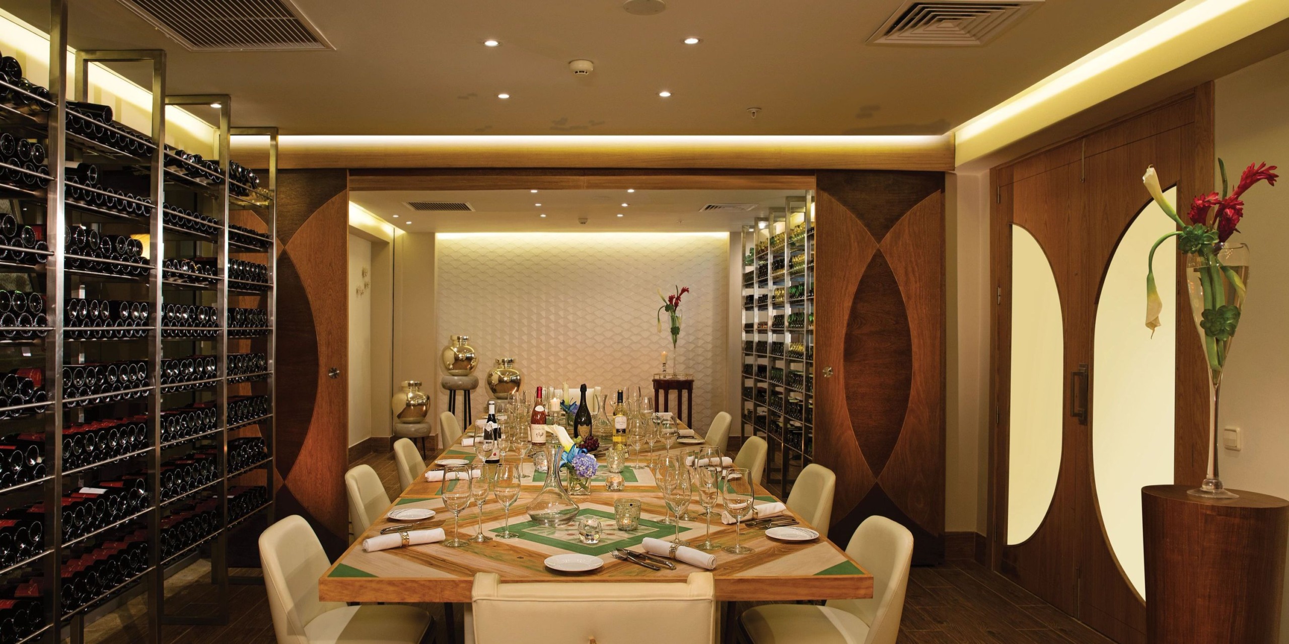 A sophisticated dining room featuring the exquisite Dreams Onyx, a long wooden table impeccably set for a meal. Wine racks adorn the walls, enhanced by elegant decor and warm lighting.