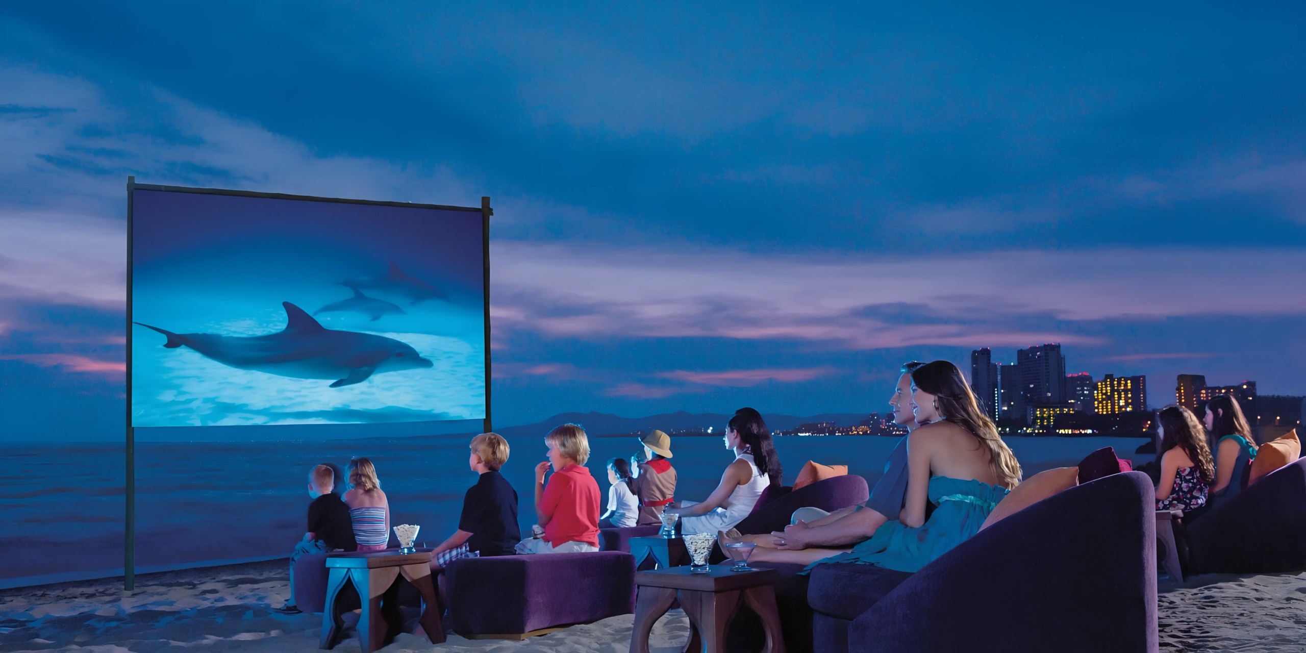 Outdoor beach movie night at Dreams Vallarta Bay with people watching a wedding film featuring dolphins.