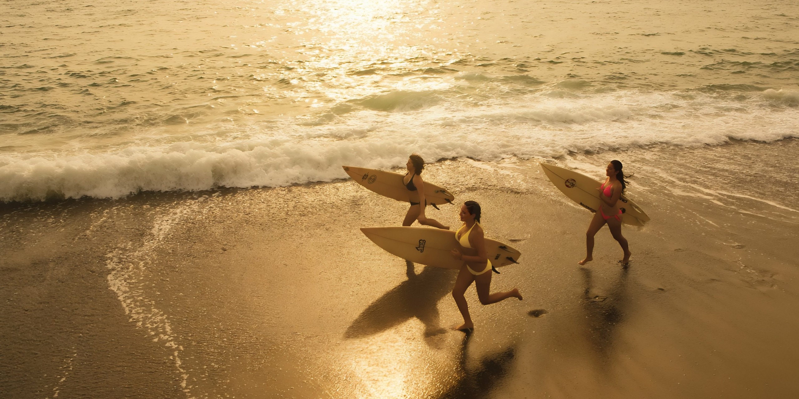 Three surfers running toward the sea with their Dreams Vallarta Bay boards at sunset for a destify wedding.