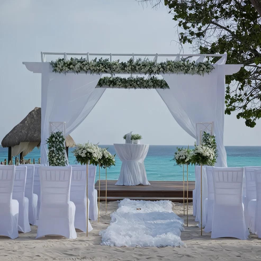 An outdoor wedding setup on a beach with a decorated archway, white chairs, and floral arrangements overlooking the ocean.