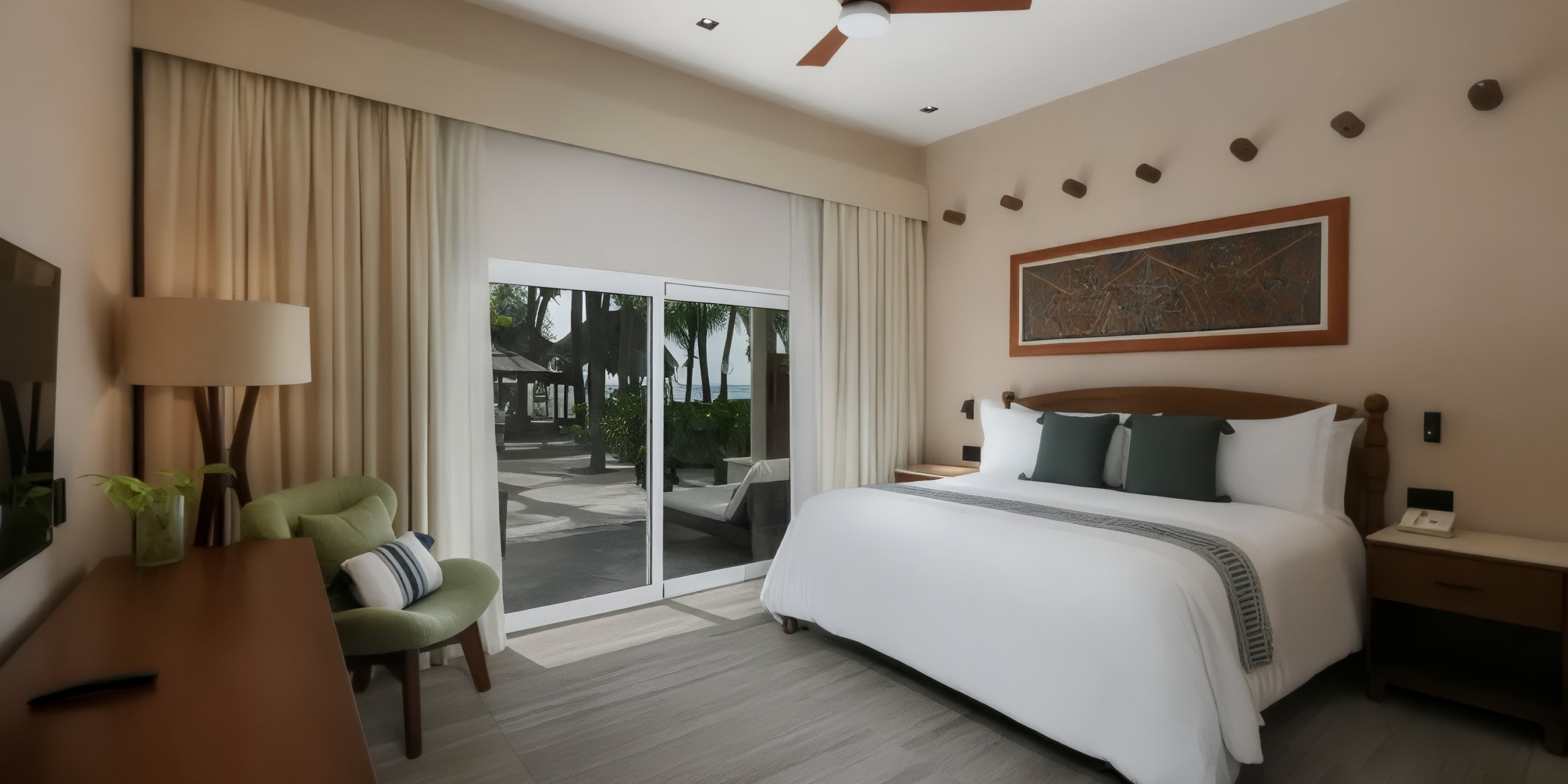 The El Dorado Maroma offers a spacious hotel room with a large bed, wooden furnishings, a seating area, and a sliding glass door that opens to an outdoor patio where trees are visible.
