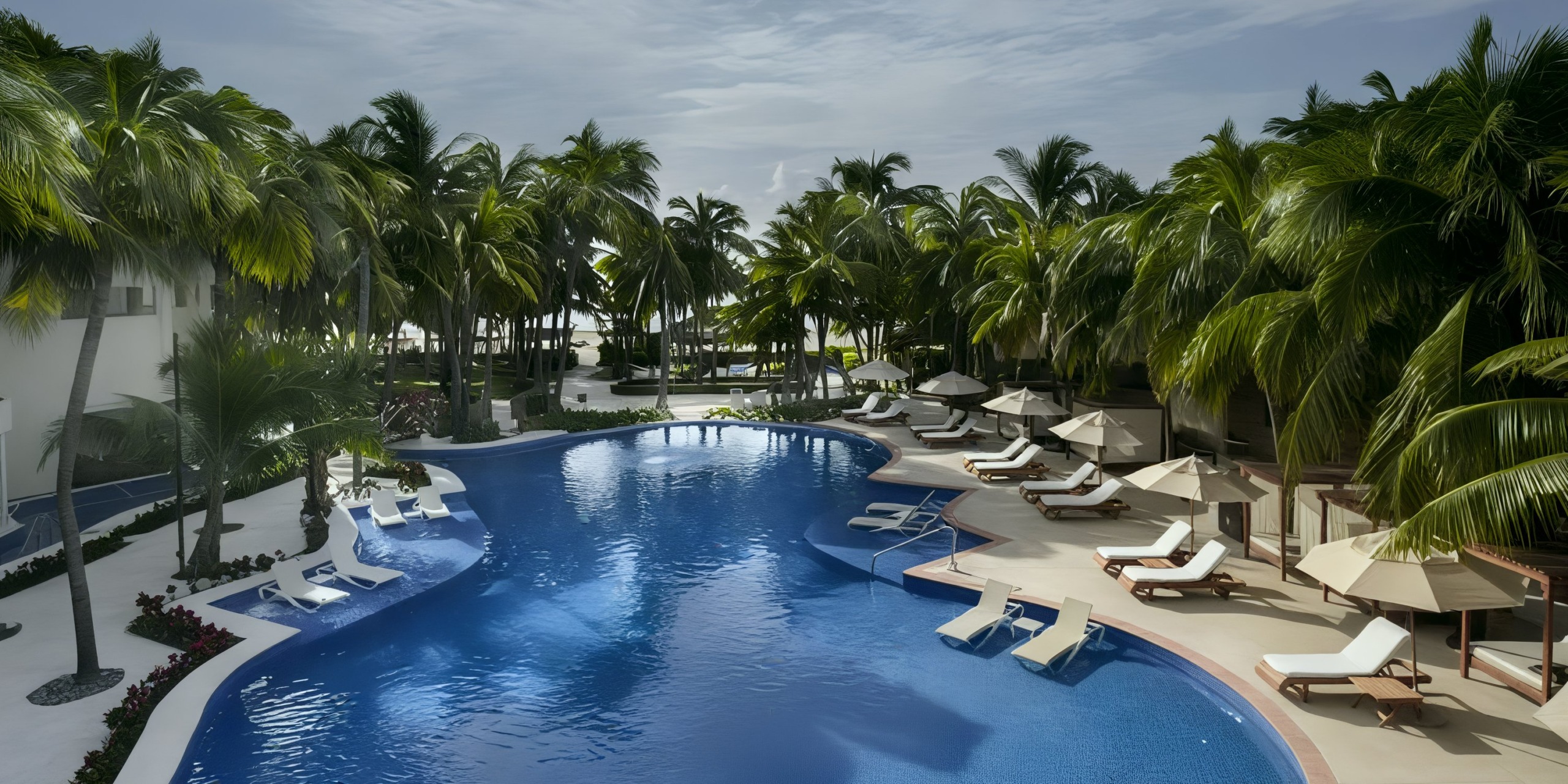 The El Dorado Maroma features a picturesque pool encircled by palm trees and equipped with lounge chairs complete with umbrellas.