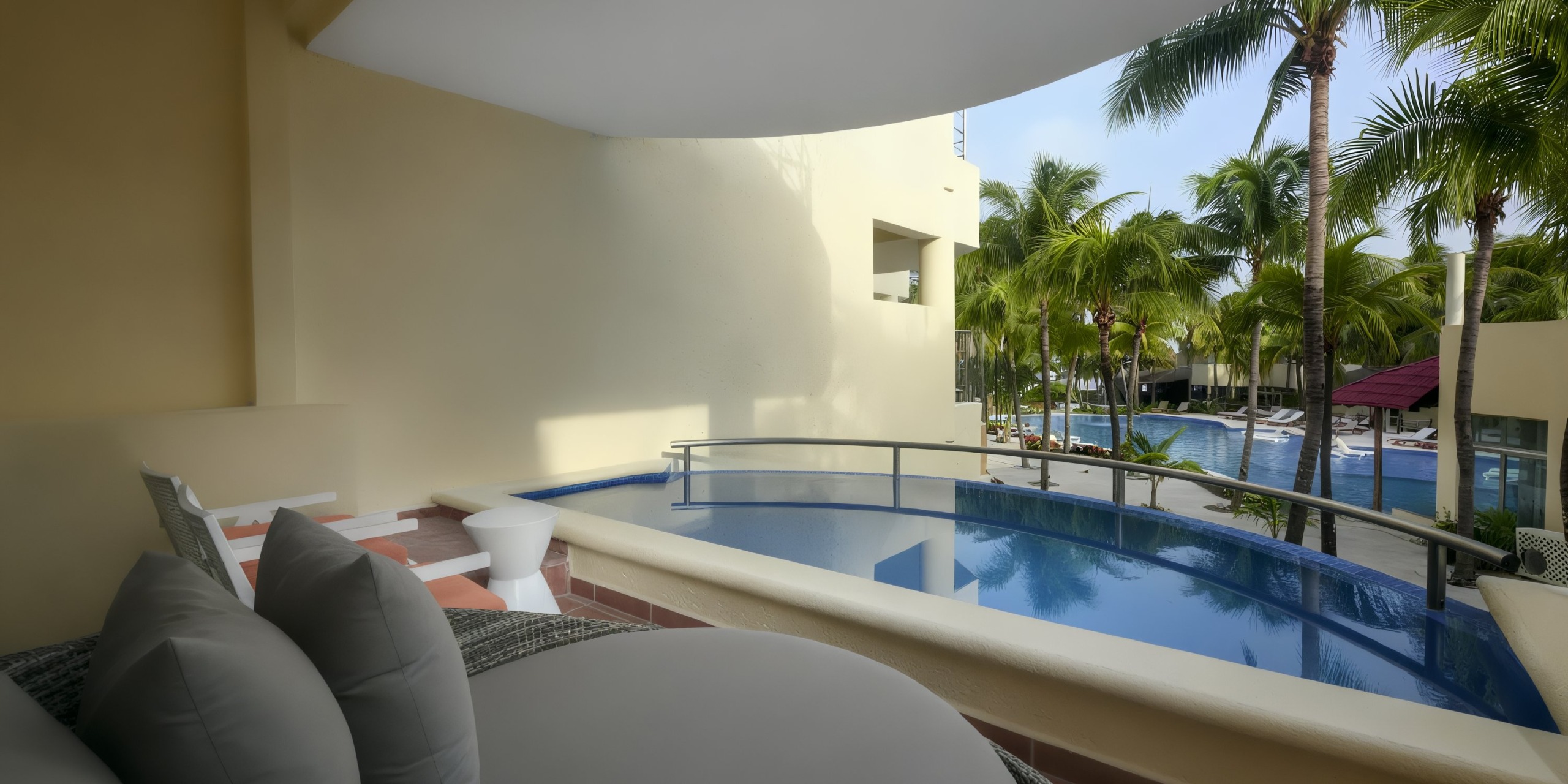The balcony at El Dorado Maroma features a small private pool with a view overlooking a larger pool encircled by palm trees.