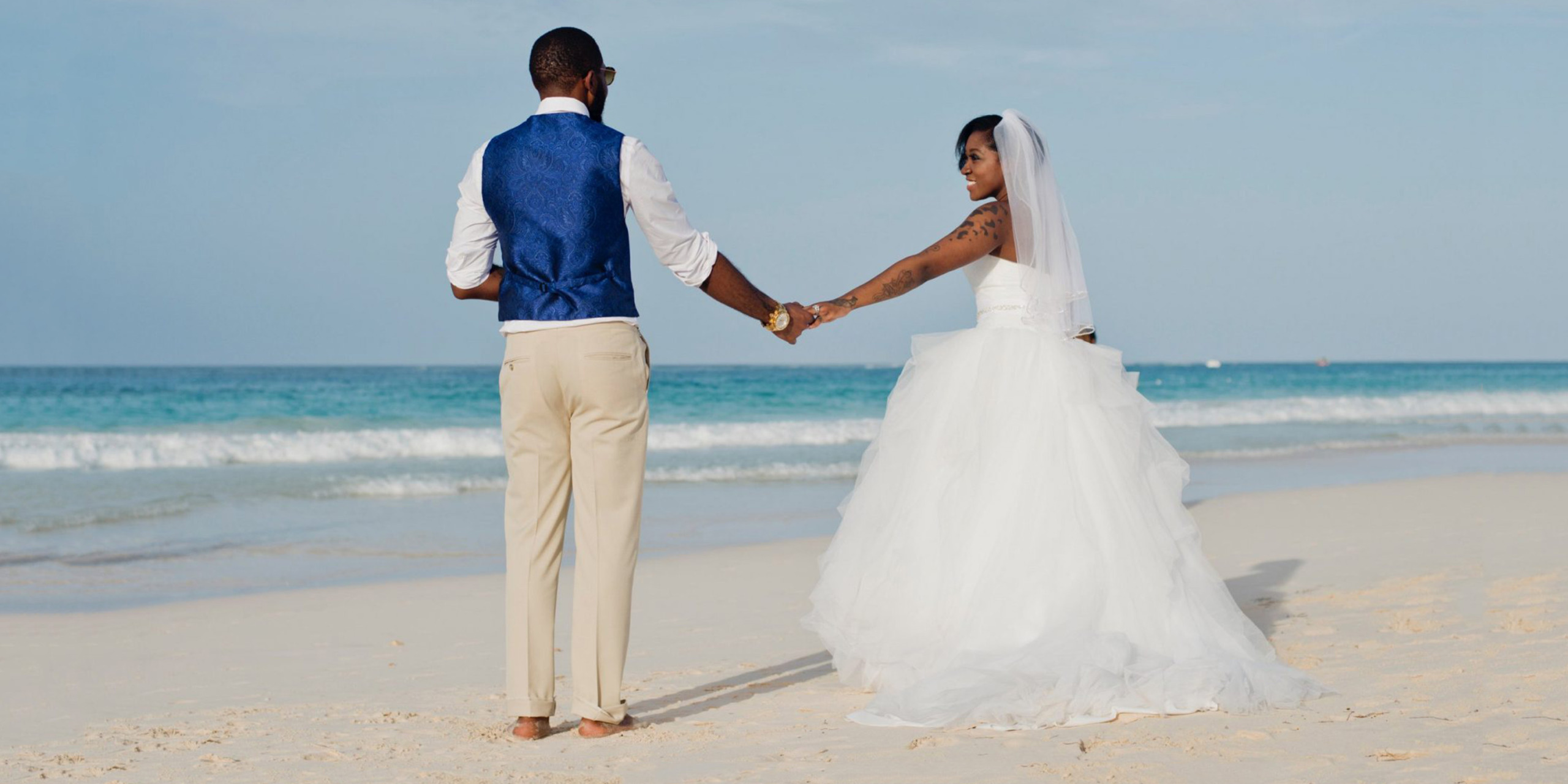 Newlywed bride and groom Felisa and Jeremiah hold hands in love on the beach during their destination wedding