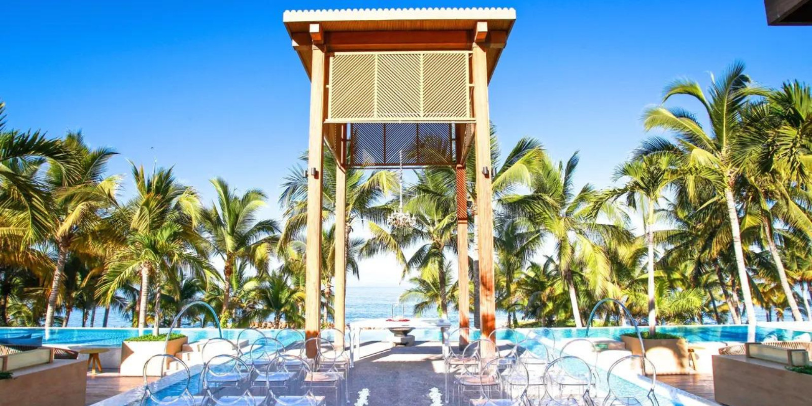 A wedding ceremony set up at Fiesta Americana Puerto Vallarta, in front of a pool and palm trees.