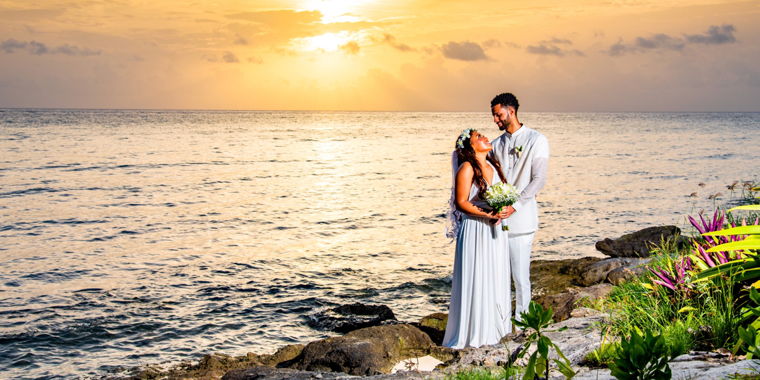 Gabby and Steven stand together in an embrace during Sunset with bouquet during their dream destination wedding