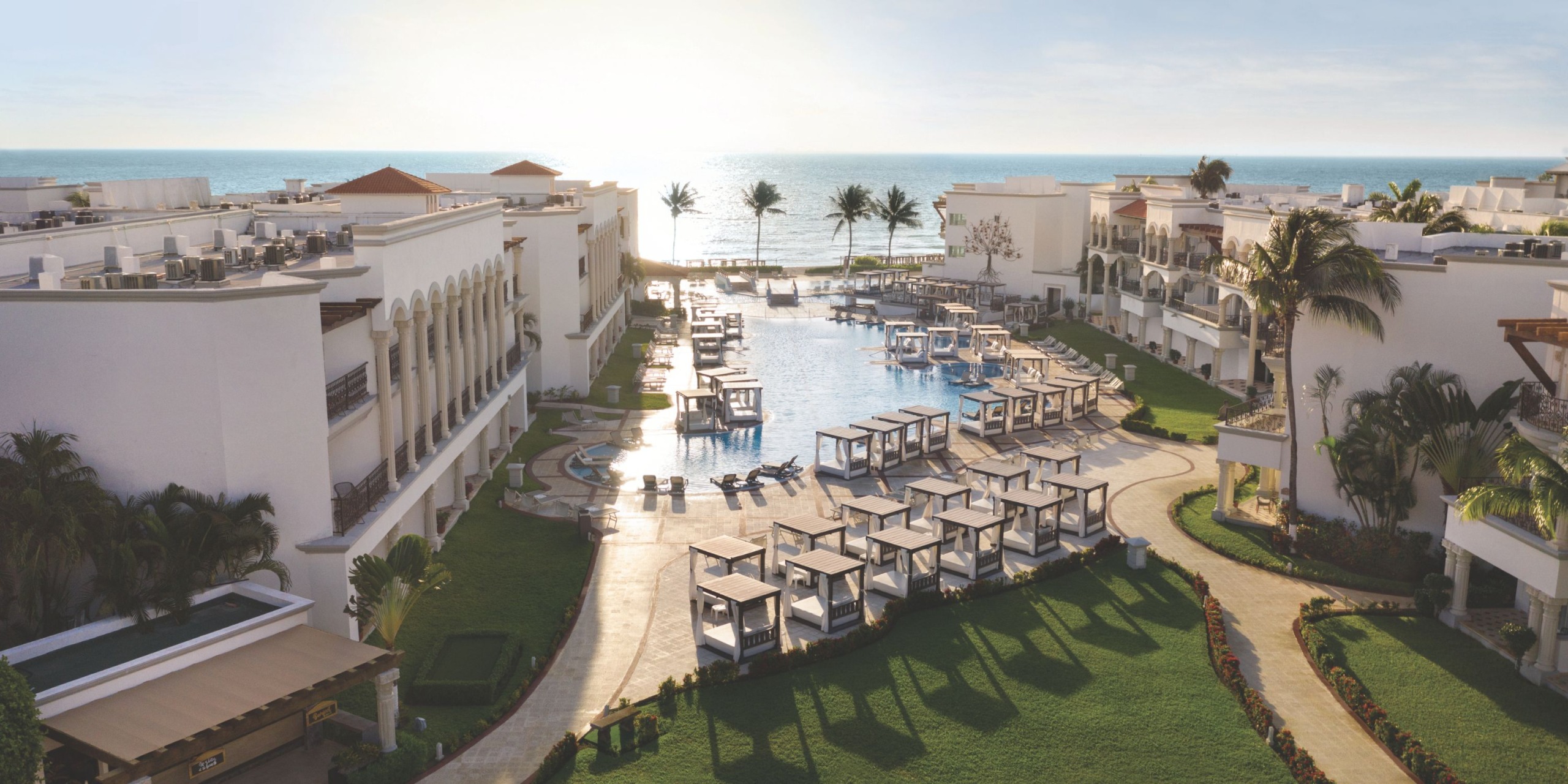 Hilton Playa del Carmen is a luxurious beachfront resort featuring a large central pool, surrounded by white buildings and palm trees, with stunning ocean views.