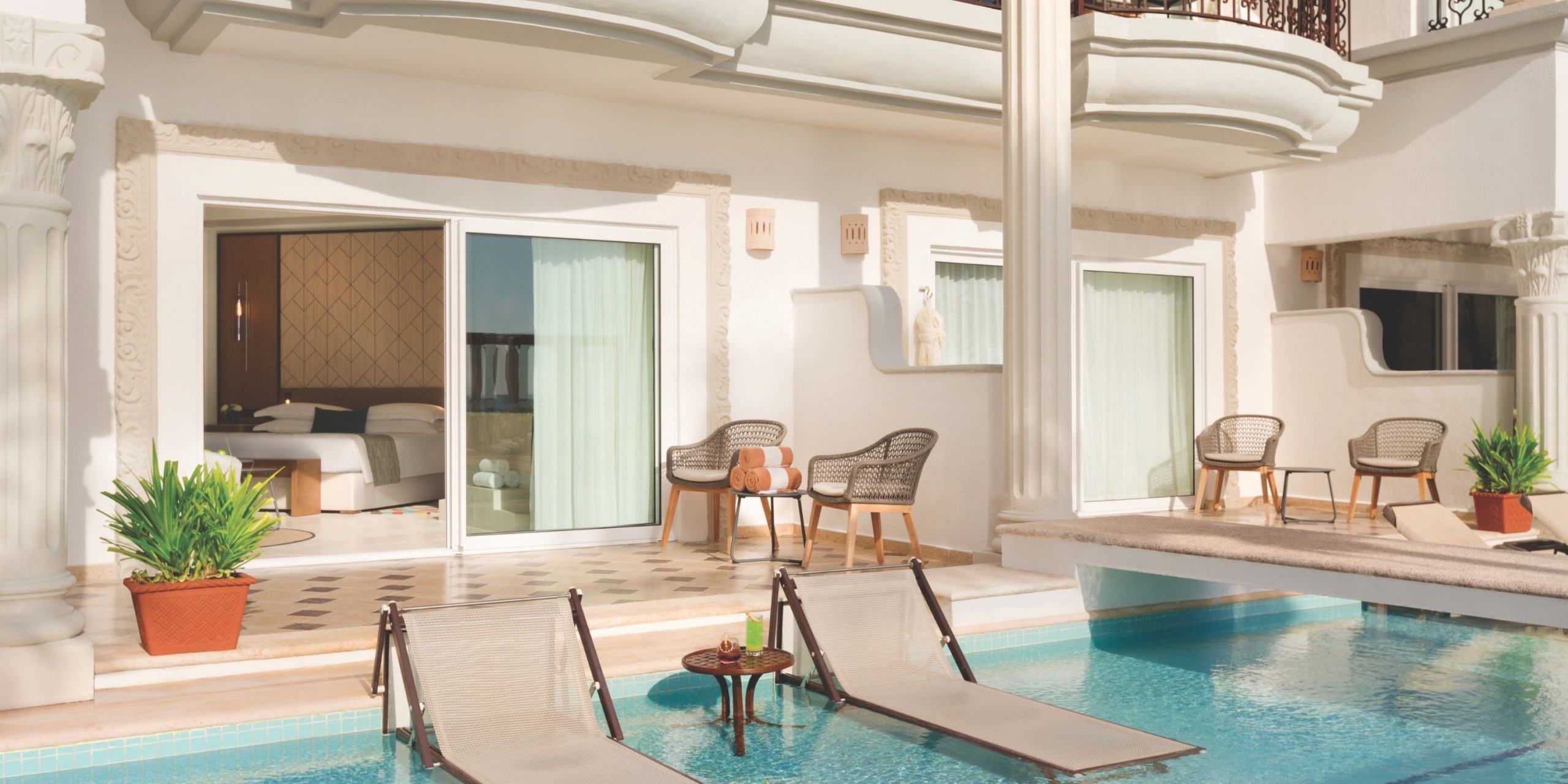 Experience the luxury of the Hilton Playa del Carmen with a poolside suite featuring two in-water lounge chairs, a poolside table, and an open sliding door that unveils a plush bedroom.