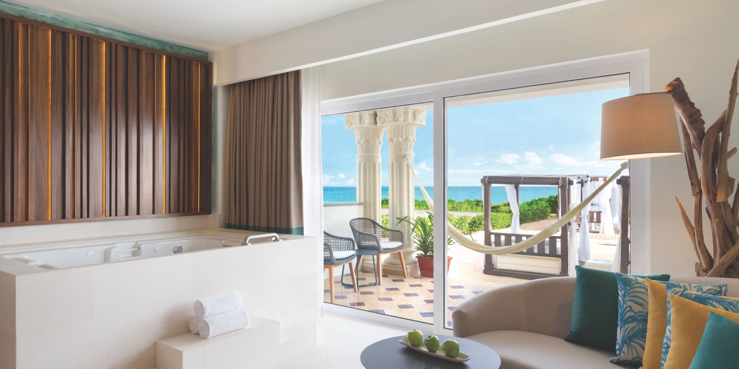 Experience a luxurious stay in a modern room at Hilton Playa del Carmen, complete with a jacuzzi, cozy seating area, and sliding glass doors that open to a private patio with stunning ocean views and a hammock for ultimate relaxation.