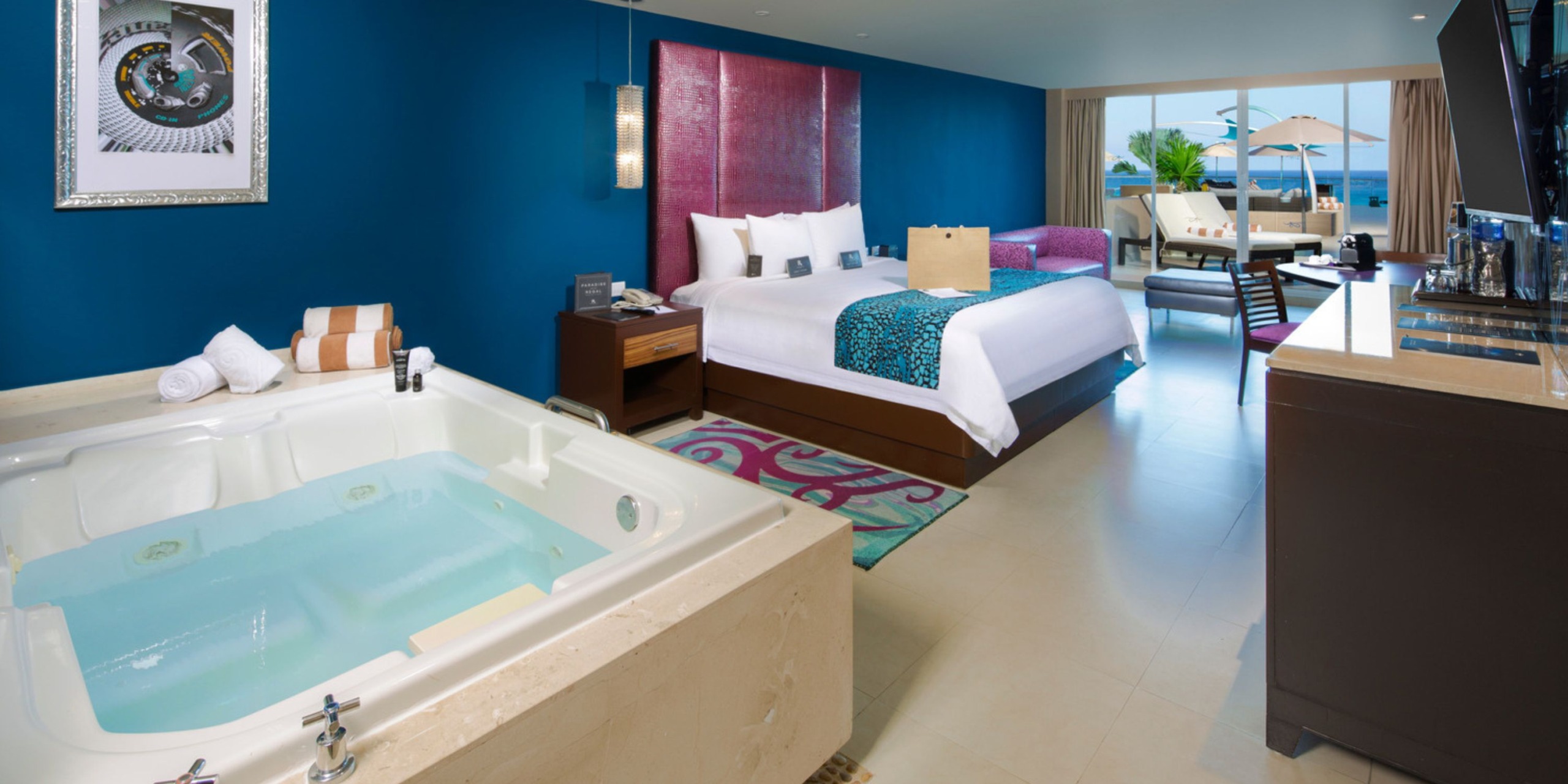 Luxurious accommodations at Hard Rock Cancun featuring a king-sized bed, a jacuzzi, and a balcony with views overlooking the swimming pool and sun loungers.