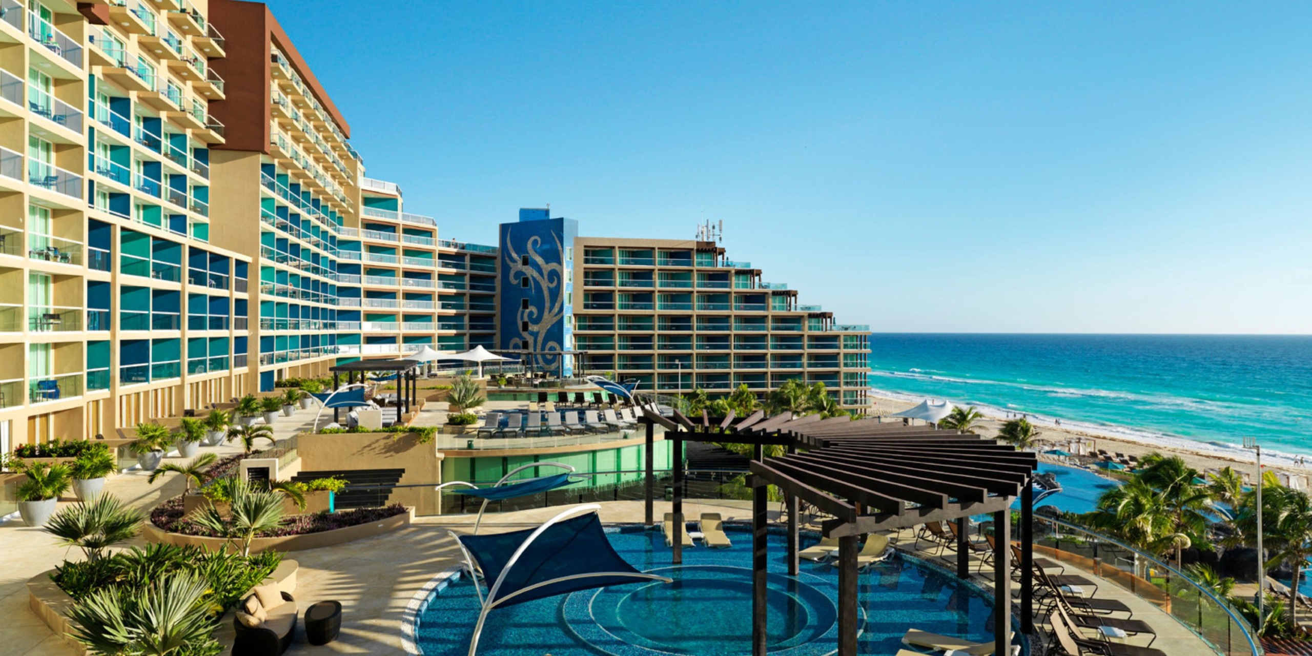 The Hard Rock Cancun features multiple balconies that overlook a pool area complete with shaded seating and stunning ocean views.