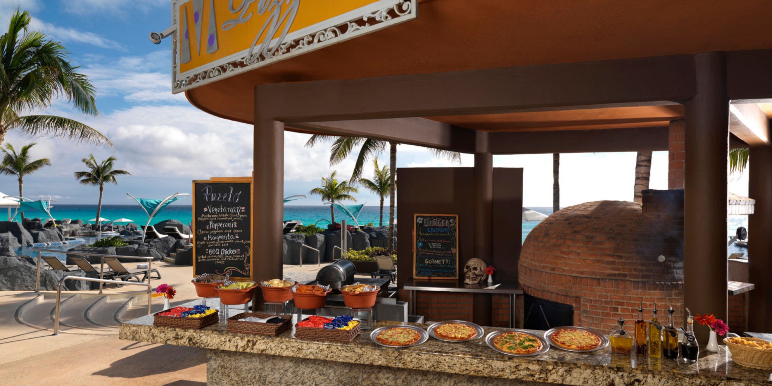The Hard Rock Cancun boasts an outdoor pizza stand by the beach, complete with a brick oven, chalkboard menu, and an appetizing display of pizzas. In the backdrop, you'll find stunning views of palm trees and the ocean.