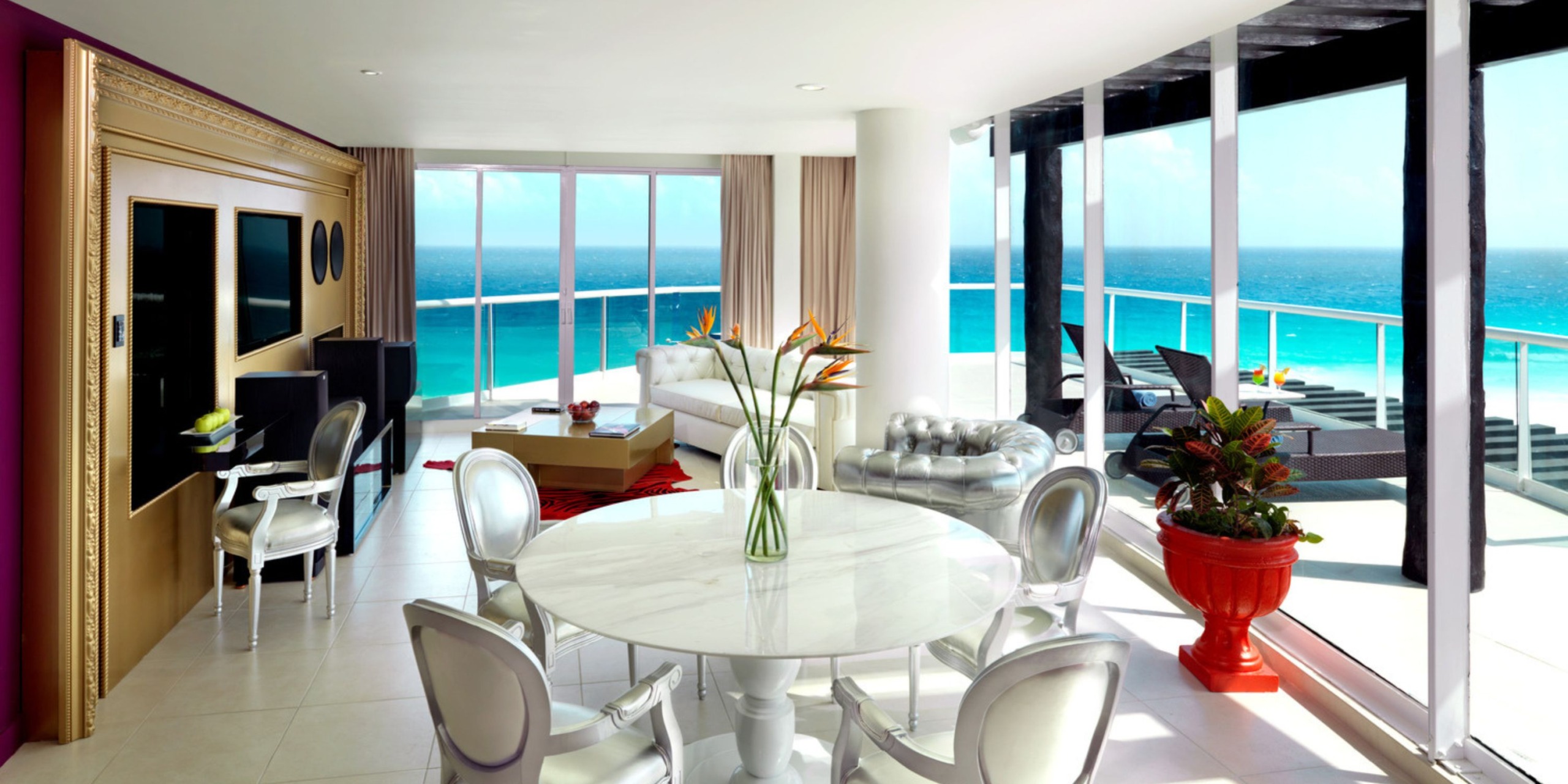 Experience an elegant and contemporary living space at Hard Rock Cancun, featuring brightly lit interiors with sleek white furniture and a stylish round dining table. Floor-to-ceiling windows and a private balcony provide stunning views of the ocean.