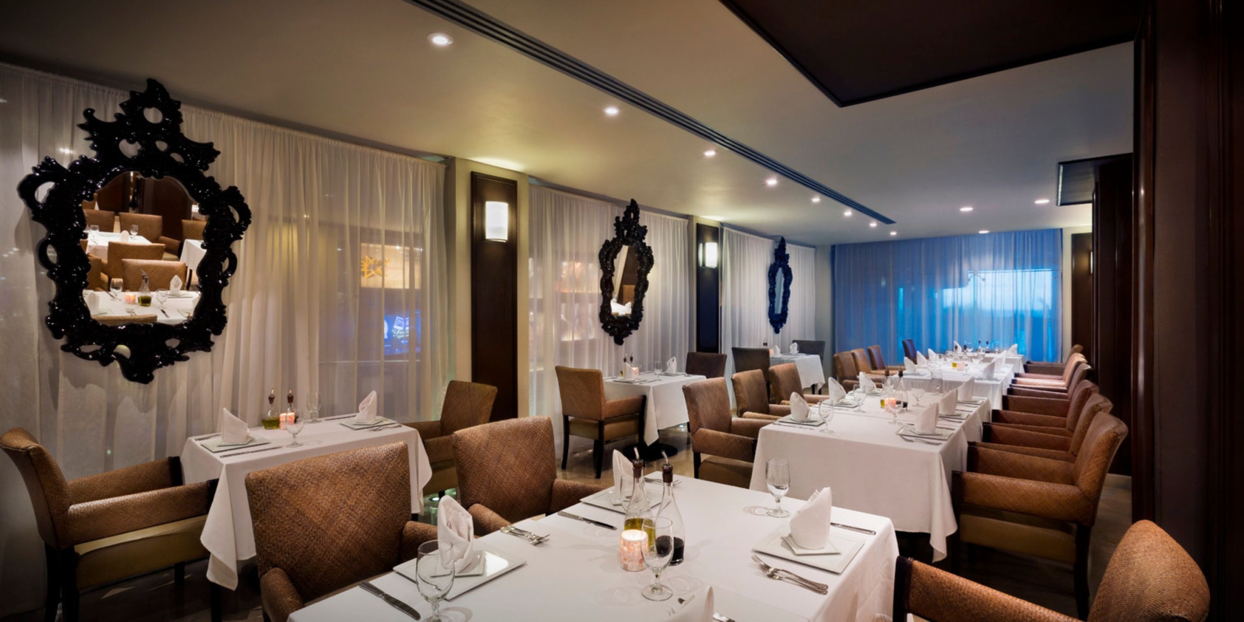 The interior of Hard Rock Cancun features elegantly arranged tables with white tablecloths, cushioned chairs, and decorative mirrors adorning the walls. The soft lighting further enhances the ambience.