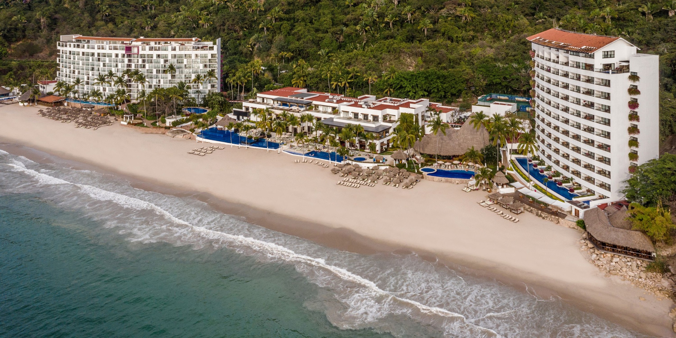 Aerial view of Hyatt Ziva Puerto Vallarta, a beachfront resort featuring pools, lounge chairs, and surrounding greenery along a sandy shore.