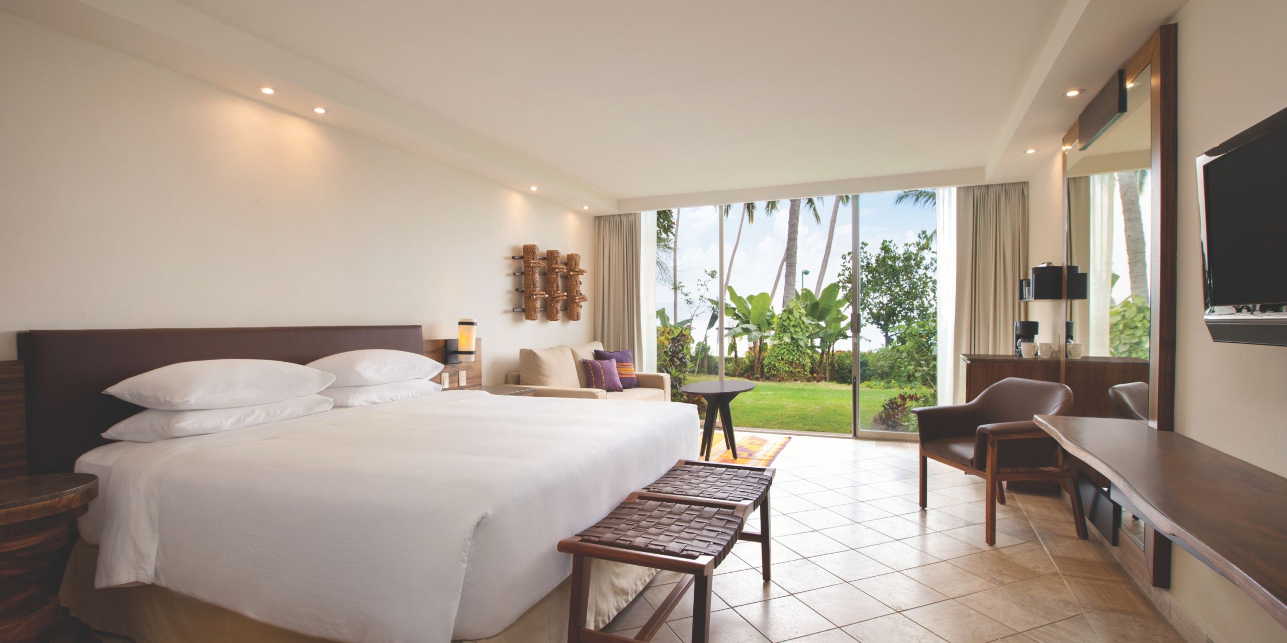 A spacious room at Hyatt Ziva Puerto Vallarta features a king-sized bed, wooden furniture, and large sliding glass doors that open to a garden view.