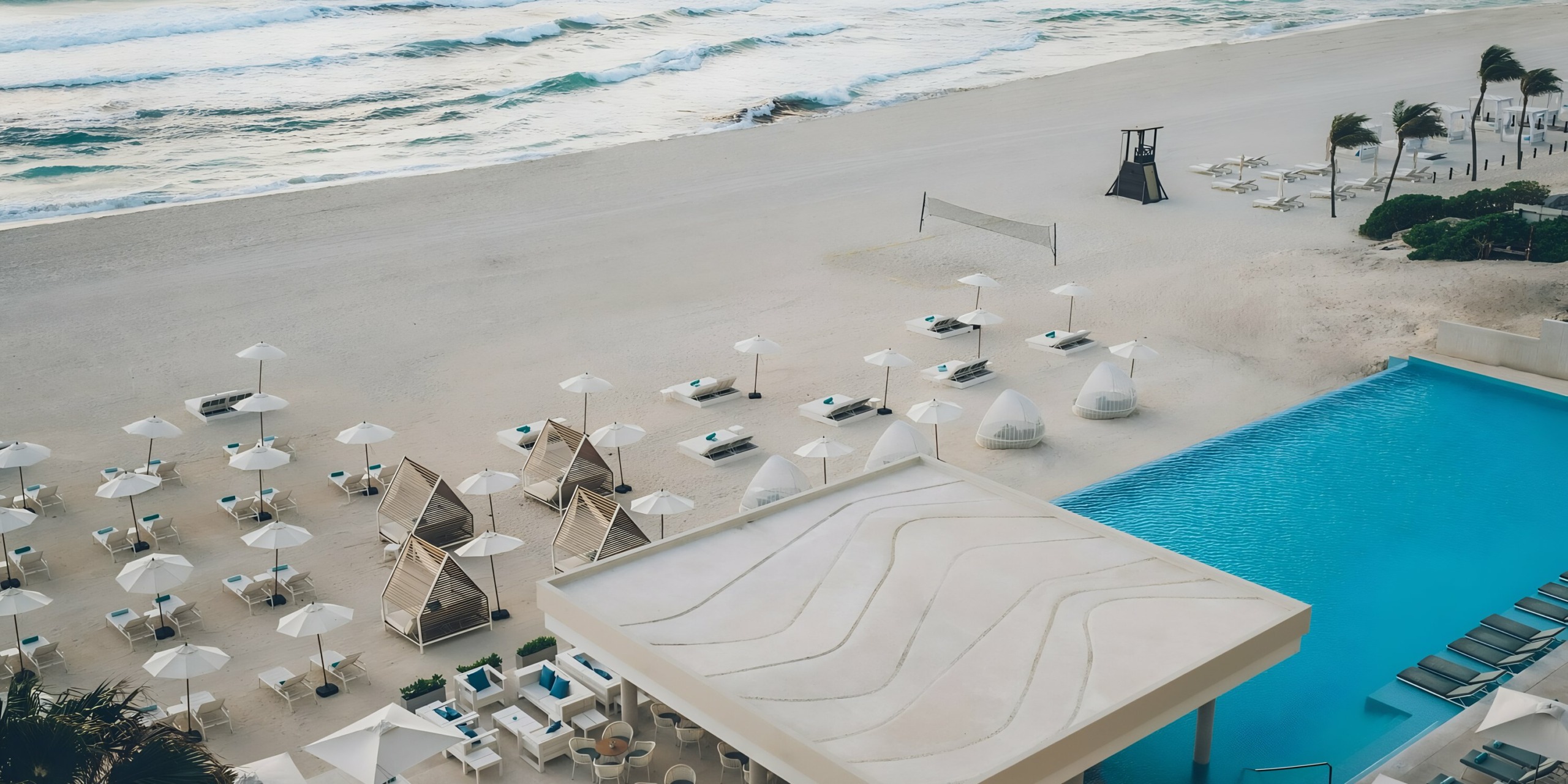 Aerial view of Iberostar Selection Cancun with an outdoor pool, sun loungers, and beach umbrellas next to a wavy sea.