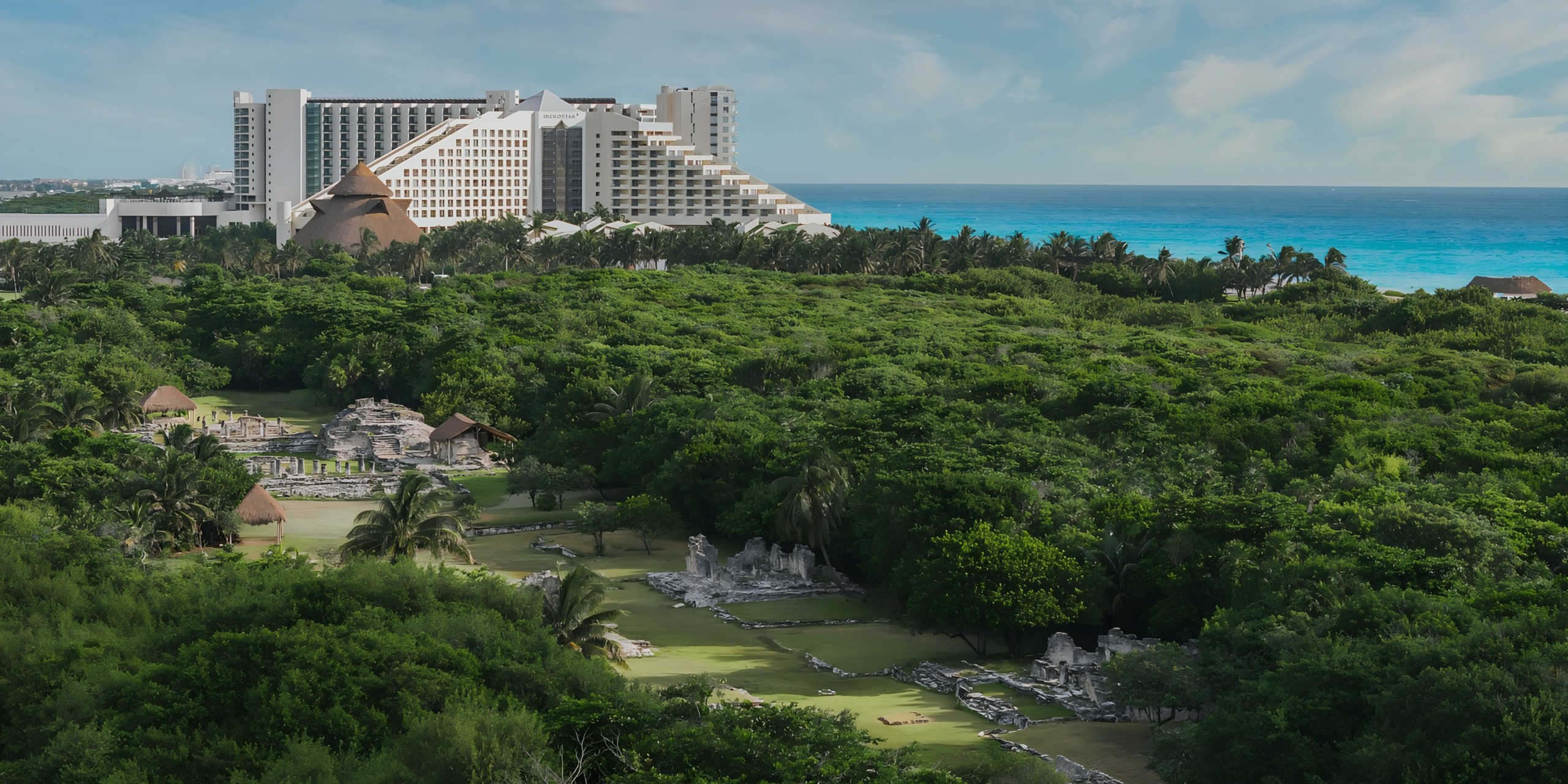 Iberostar Selection Cancun overlooking ancient ruins amidst lush greenery with a view of the turquoise sea in the background.