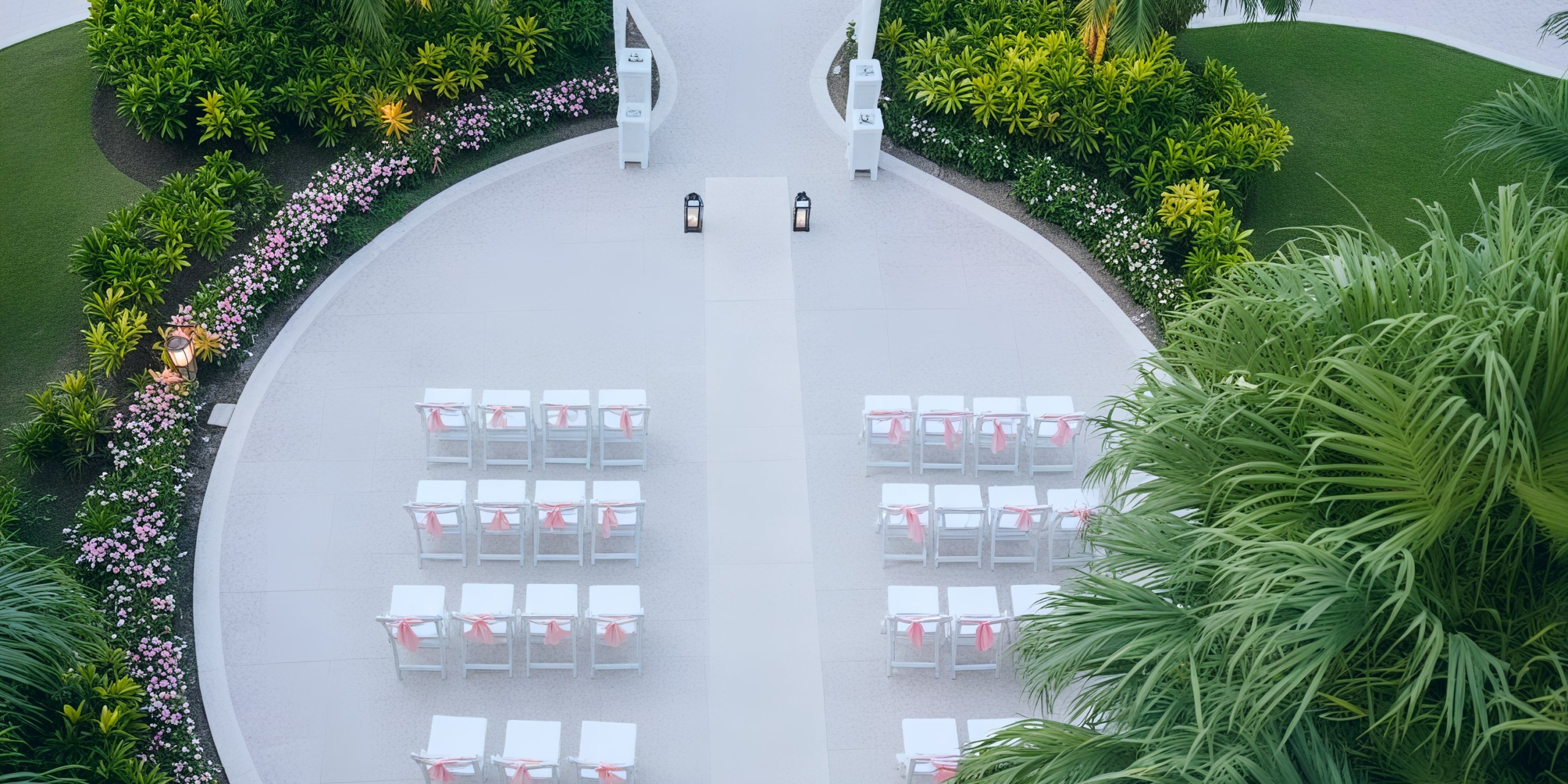 The wedding aisle at Iberostar Waves Rose Hall Beach is beautifully arranged with white chairs adorned with pink ribbons and complemented by lush greenery, creating an idyllic setting for a stunning destination wedding.