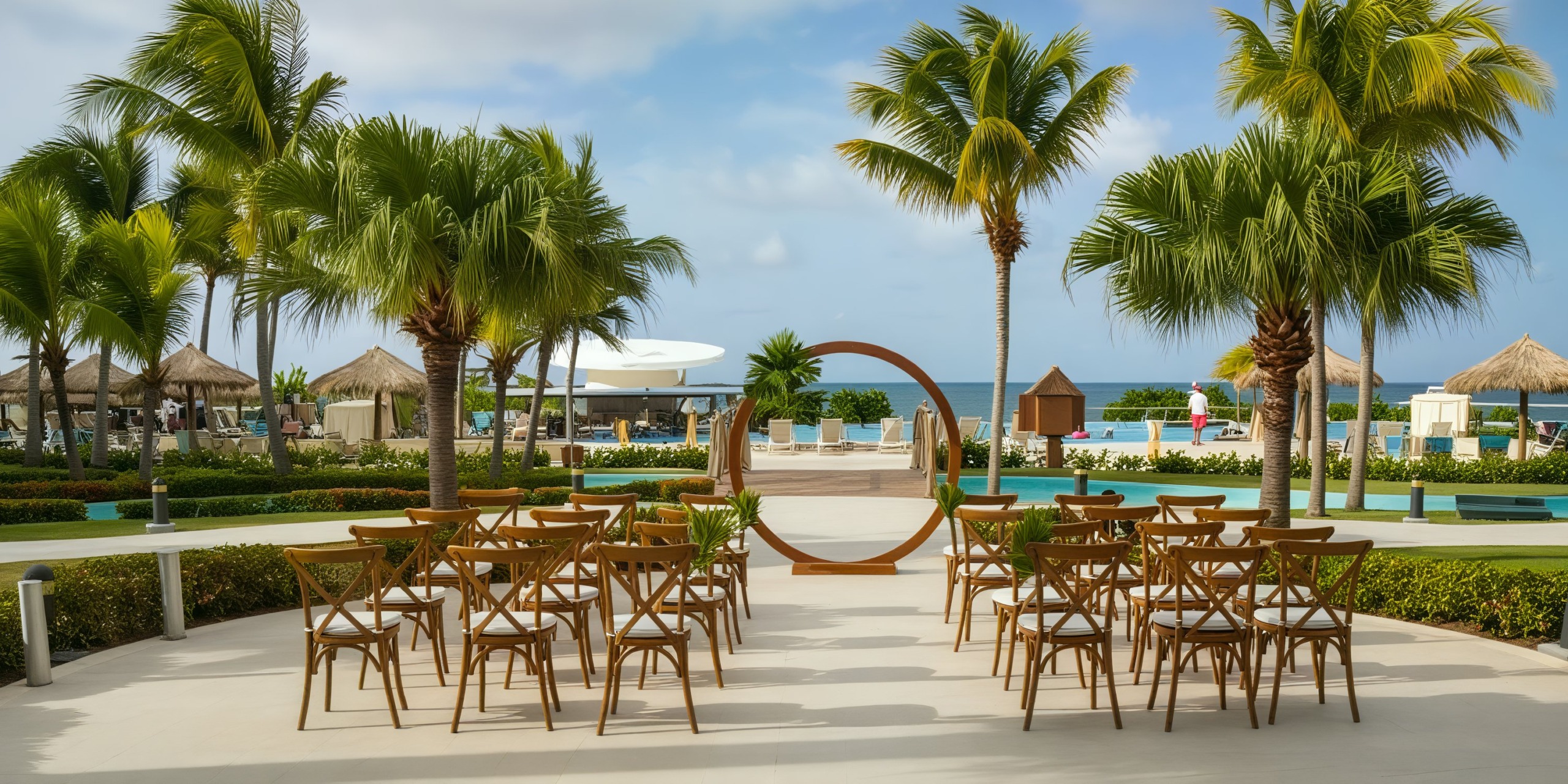 Experience a picturesque destination wedding at Iberostar Waves, featuring elegant wooden chairs and a beautiful circular arch situated by the pool.