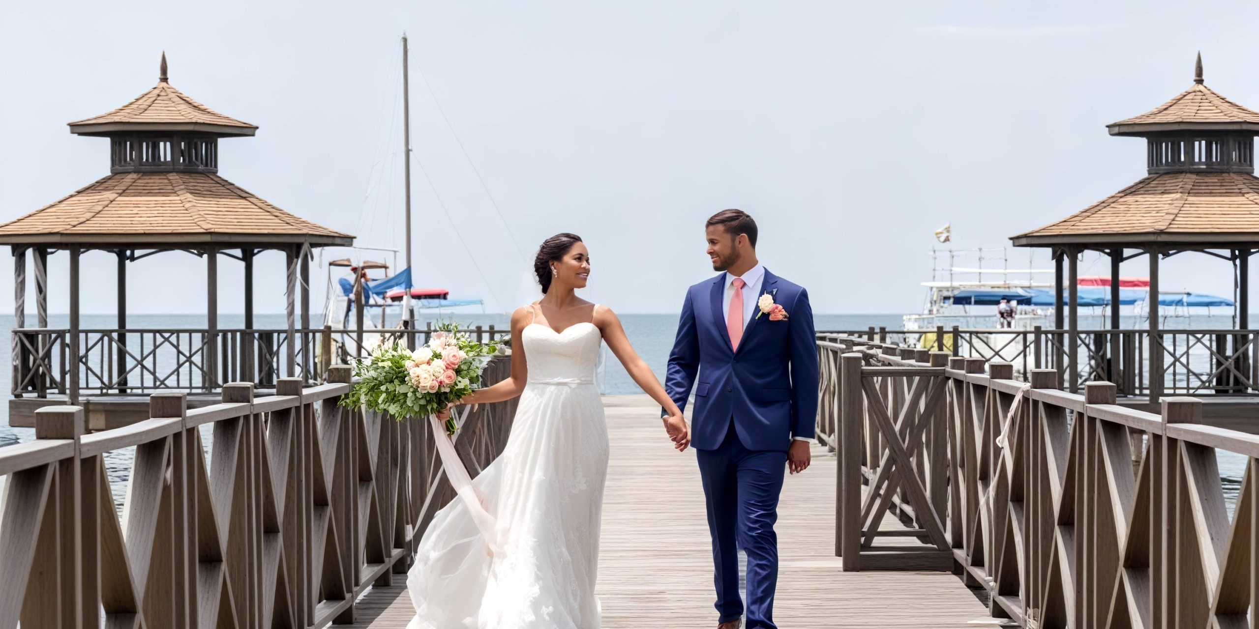 The bride and groom are holding hands as they stroll along the beach at Iberostar Waves Rose Hall, celebrating their destination wedding.