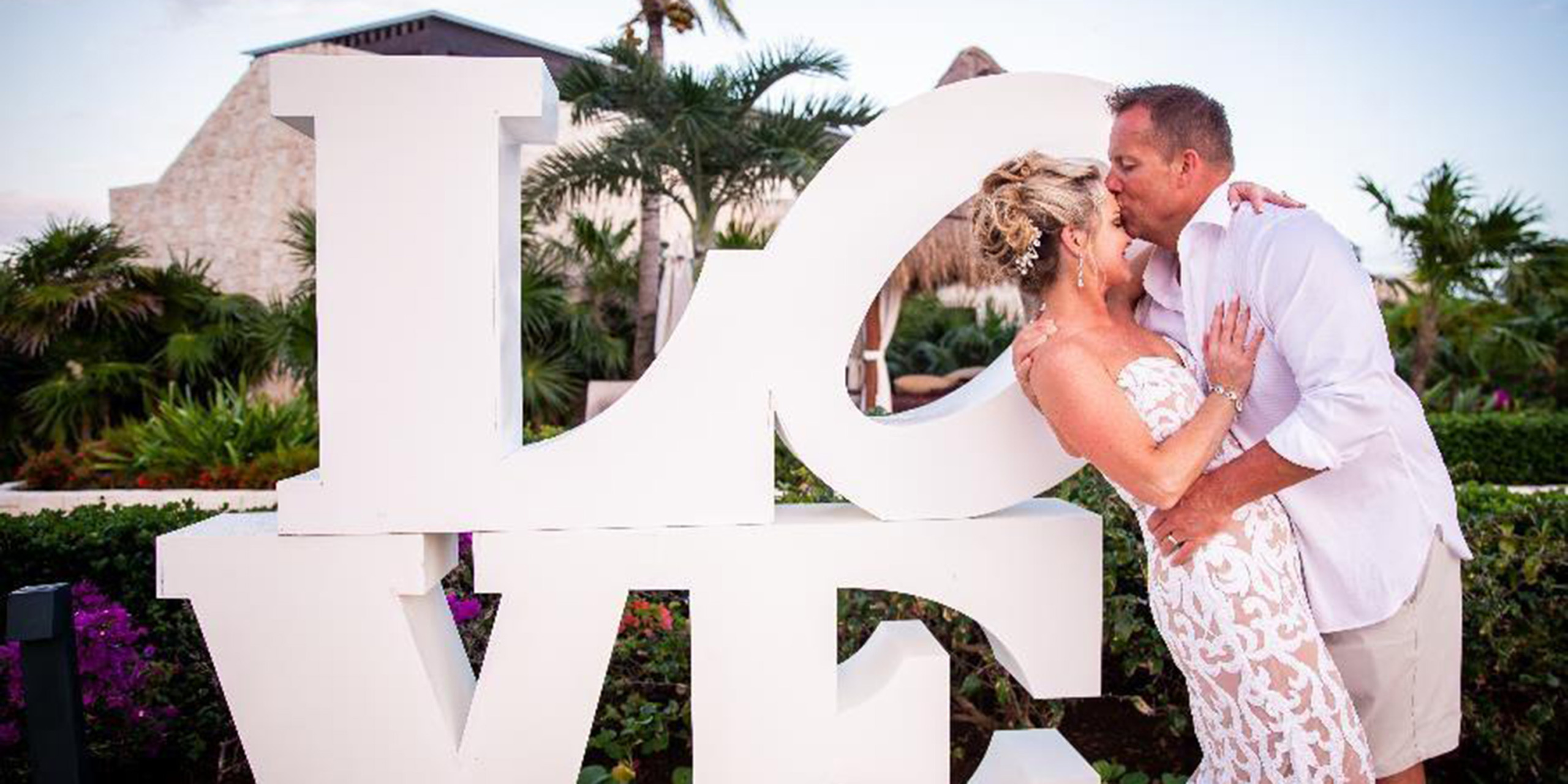 Jacqueline and Troy kiss at a LOVE statue. Love is a pop art image by American artist Robert Indiana. It consists of the letters L and O over the letters V and E in bold Didone type; the O is slanted sideways so that its oblong negative space creates a line leading to the V.