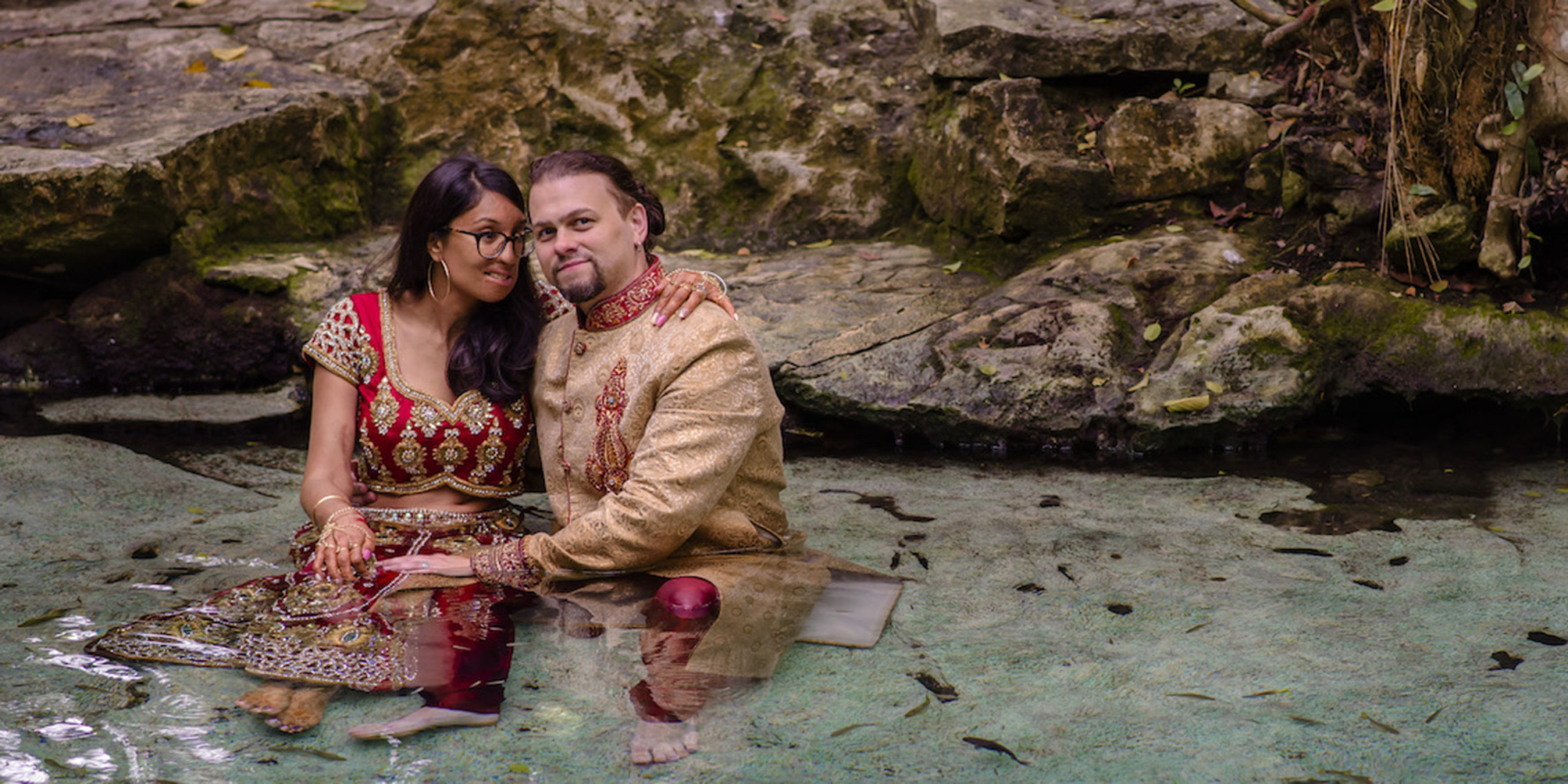 Jason and Priya embrace in the jungle in a pond