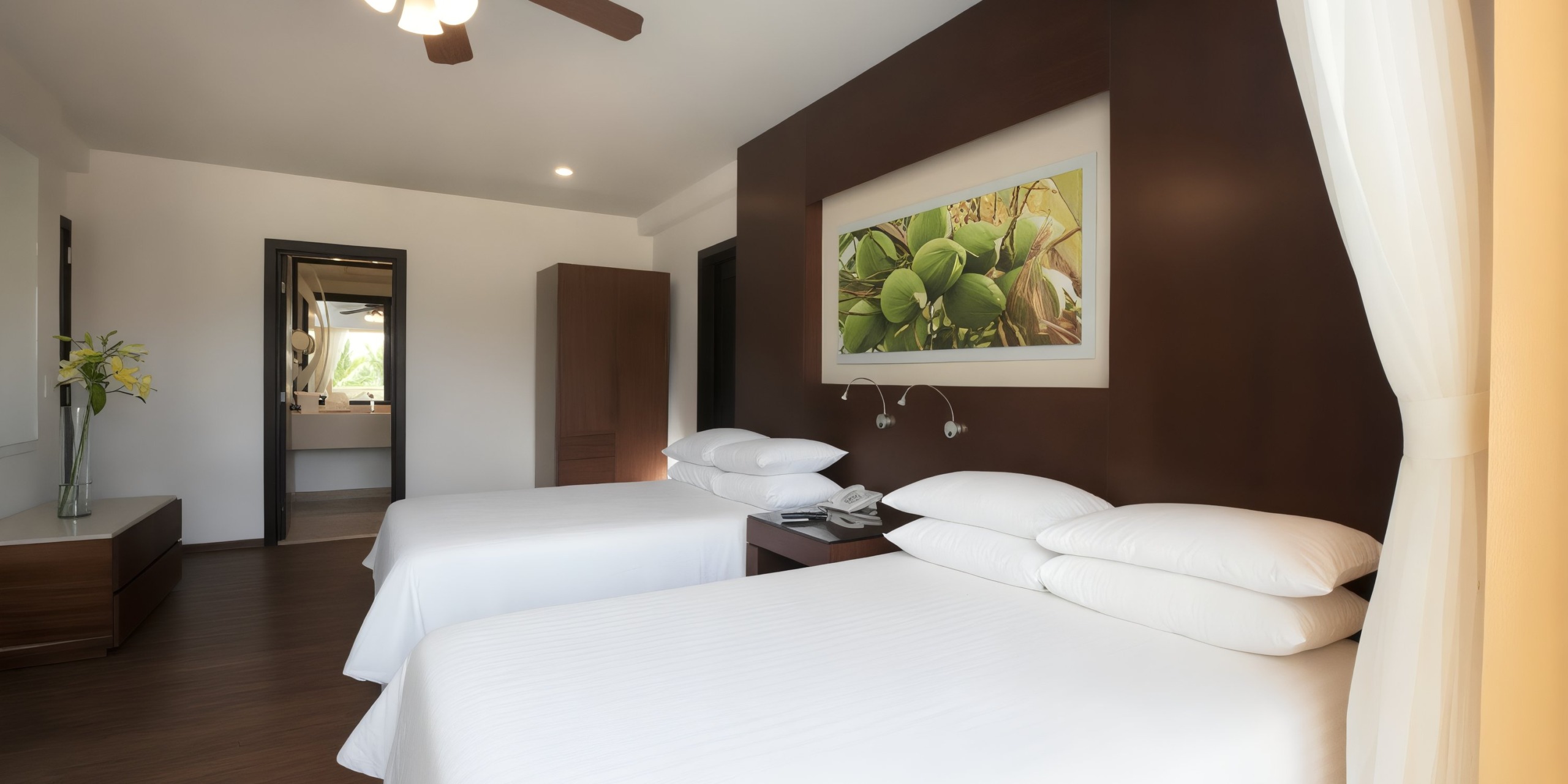 The Krystal Grand Nuevo Vallarta offers a hotel room featuring two neatly made double beds with wooden headboards, a wardrobe, and an artwork above the beds. A doorway in the background provides access to a bathroom.