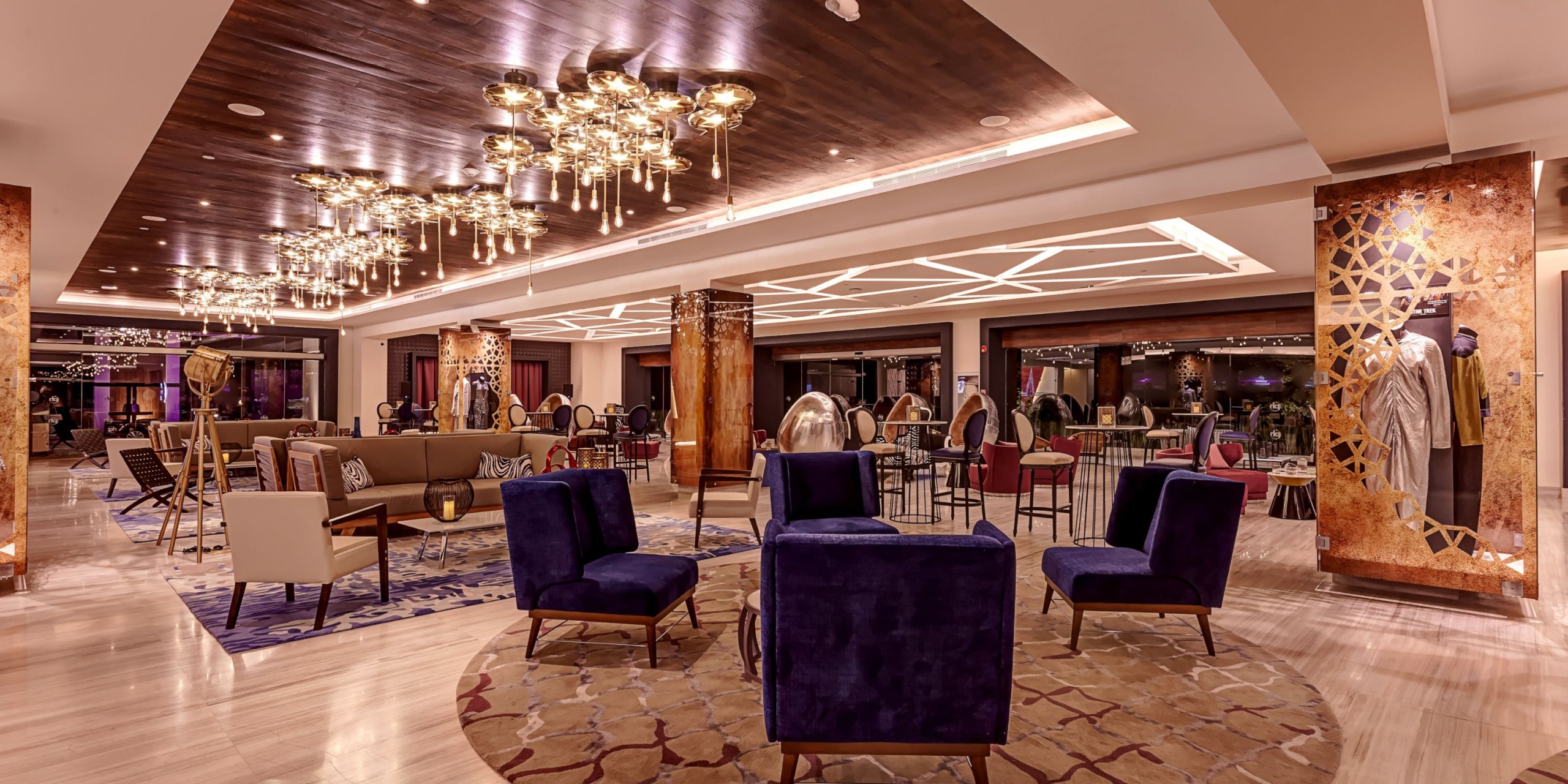 The lobby of Planet Hollywood Costa Rica is spacious and modern, featuring purple chairs, decorative lighting, and a beige carpet.