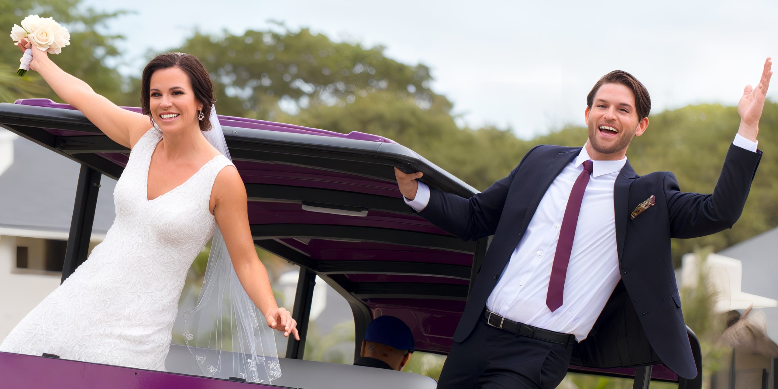 A bride and groom in wedding attire joyfully pose on a moving vehicle near Planet Hollywood Costa Rica, with the bride holding a bouquet and both smiling broadly.
