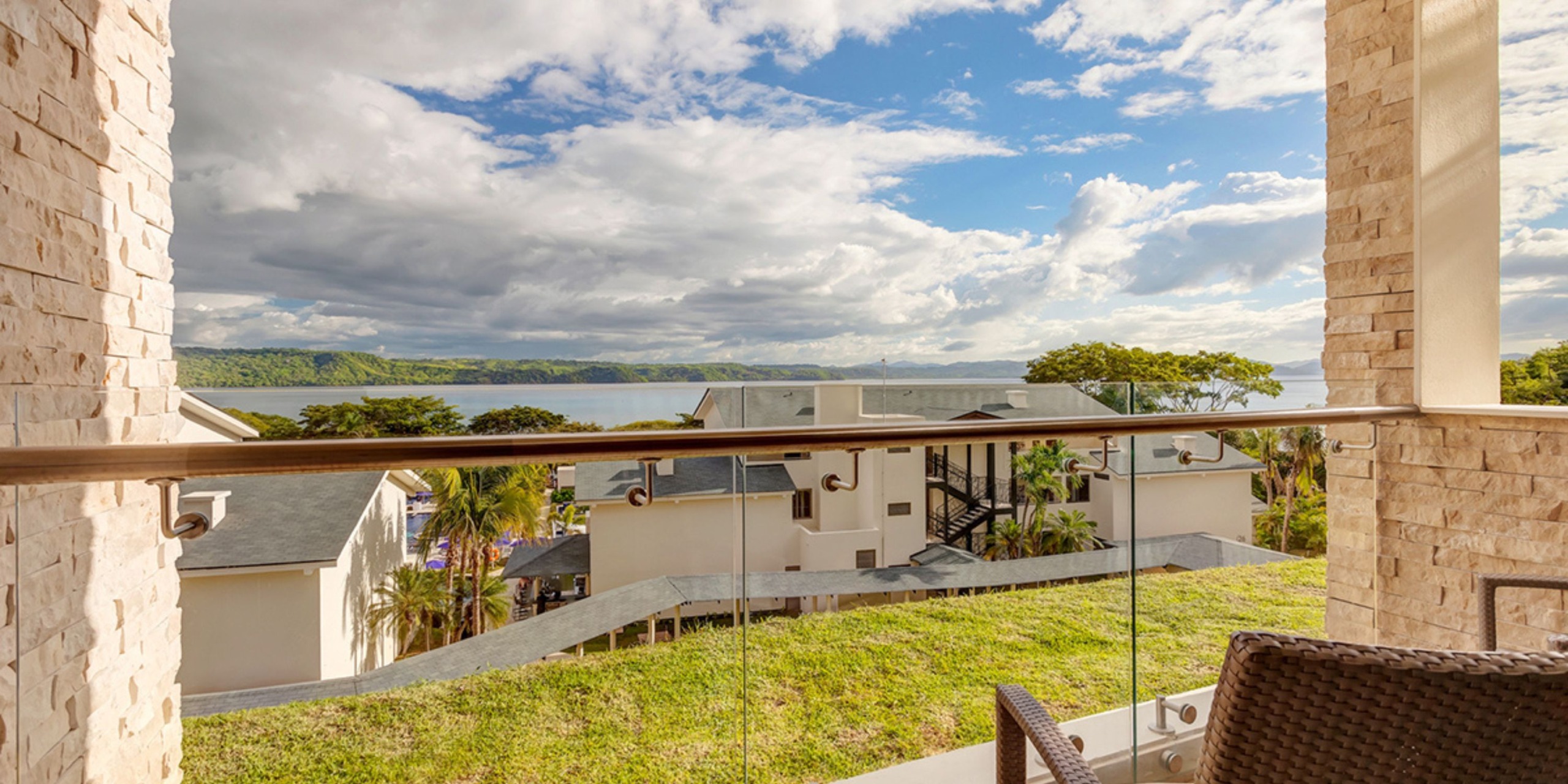 The view from a balcony at Planet Hollywood Costa Rica showcases a picturesque landscape of buildings, lush green hills, and a body of water set beneath a partly cloudy sky.
