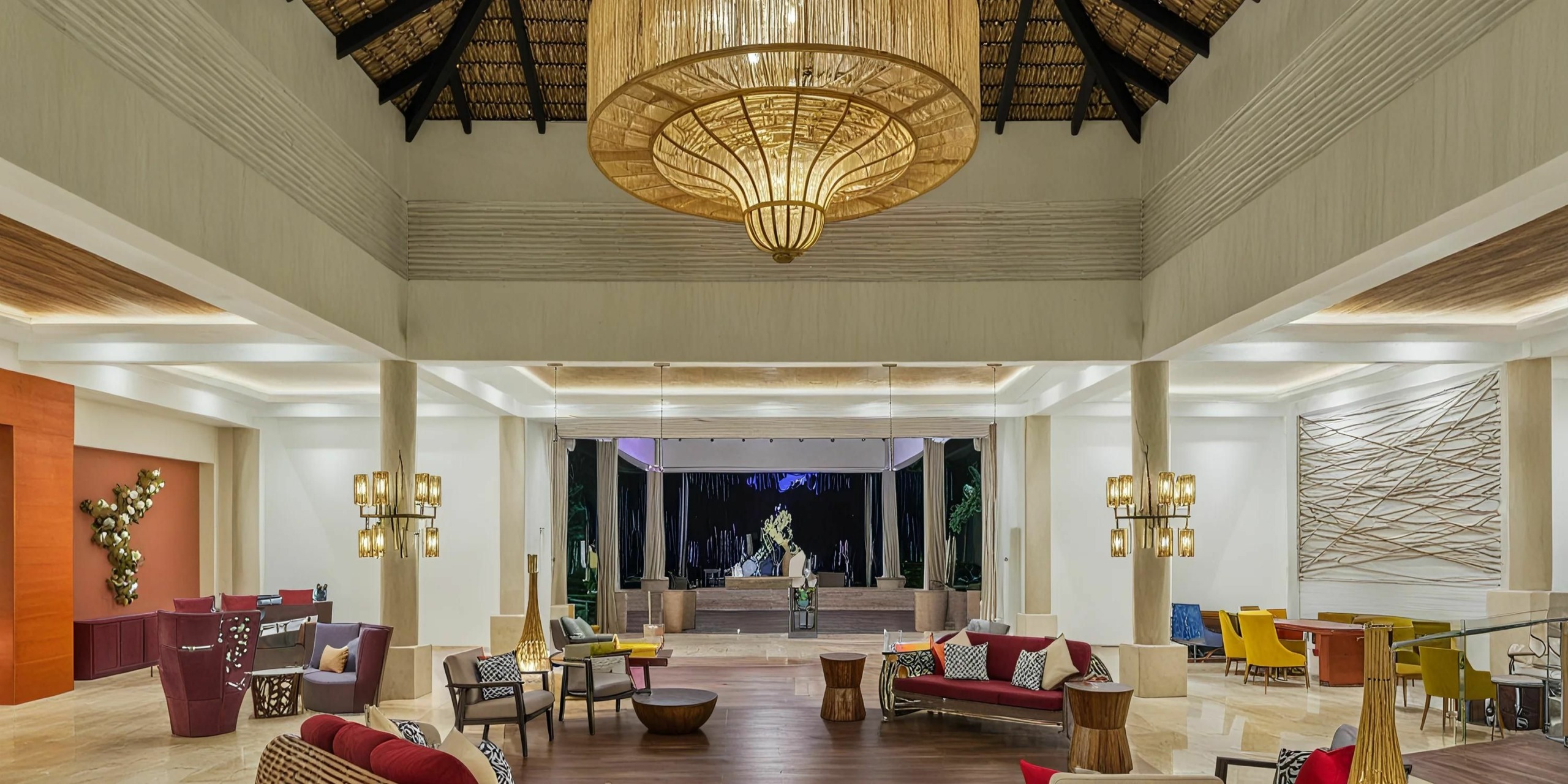 The lobby of the Royalton Punta Cana is spacious and elegantly designed with modern furniture, a grand central chandelier, and soaring high ceilings. It features multiple seating areas and expansive windows that open up to beautiful outdoor views.