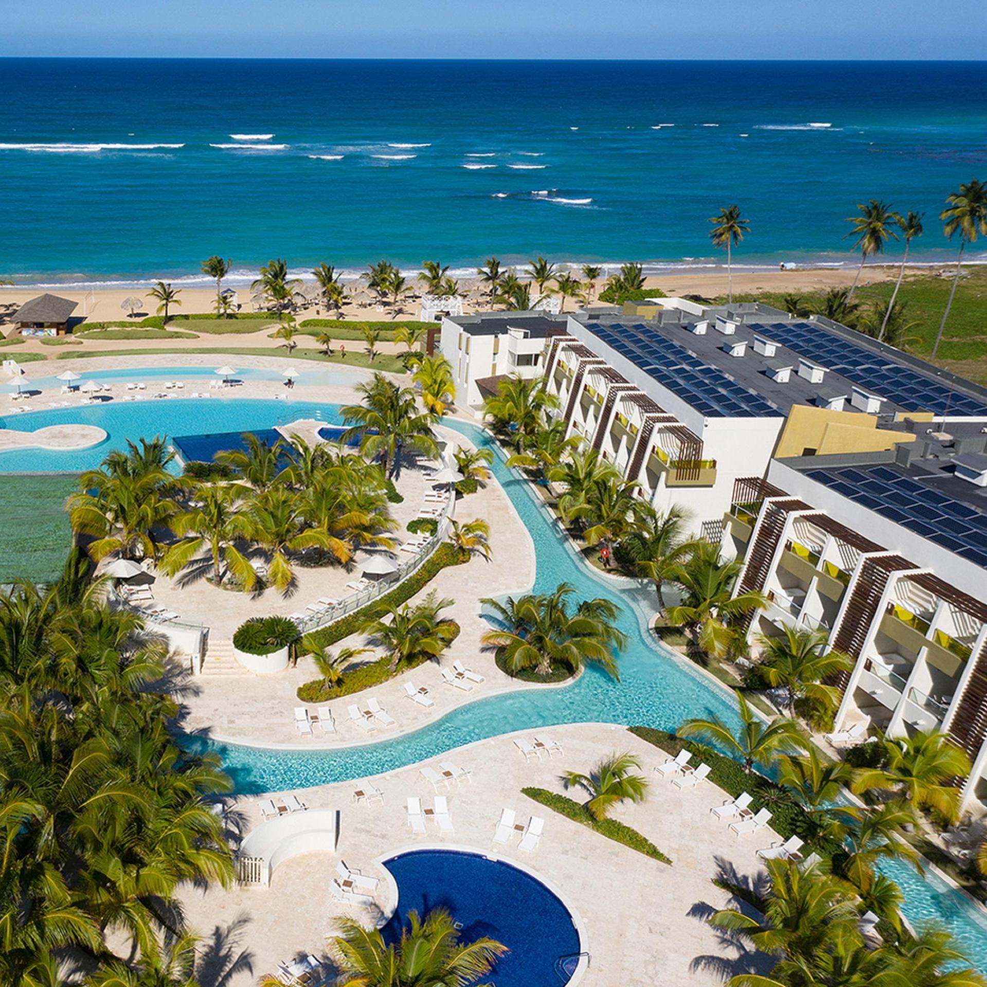 Aerial view of Dreams Onyx, a luxurious coastal resort specializing in destination weddings, with multiple swimming pools, palm trees, and an adjacent beach with clear blue waters.