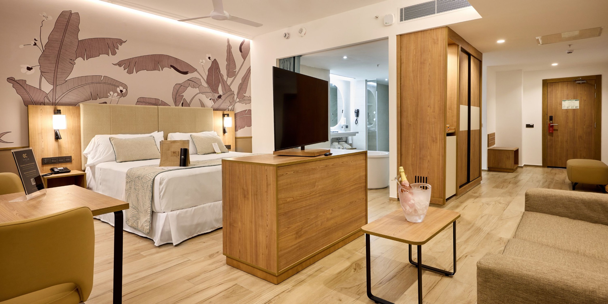 The Hotel Riu Palace Bavaro offers a contemporary suite that includes a comfortable bed, a television, a seating area, and a desk. Above the bed is an impressive mural, and you'll find a bottle of champagne waiting on the table. The room is elegantly enhanced with wood accents.