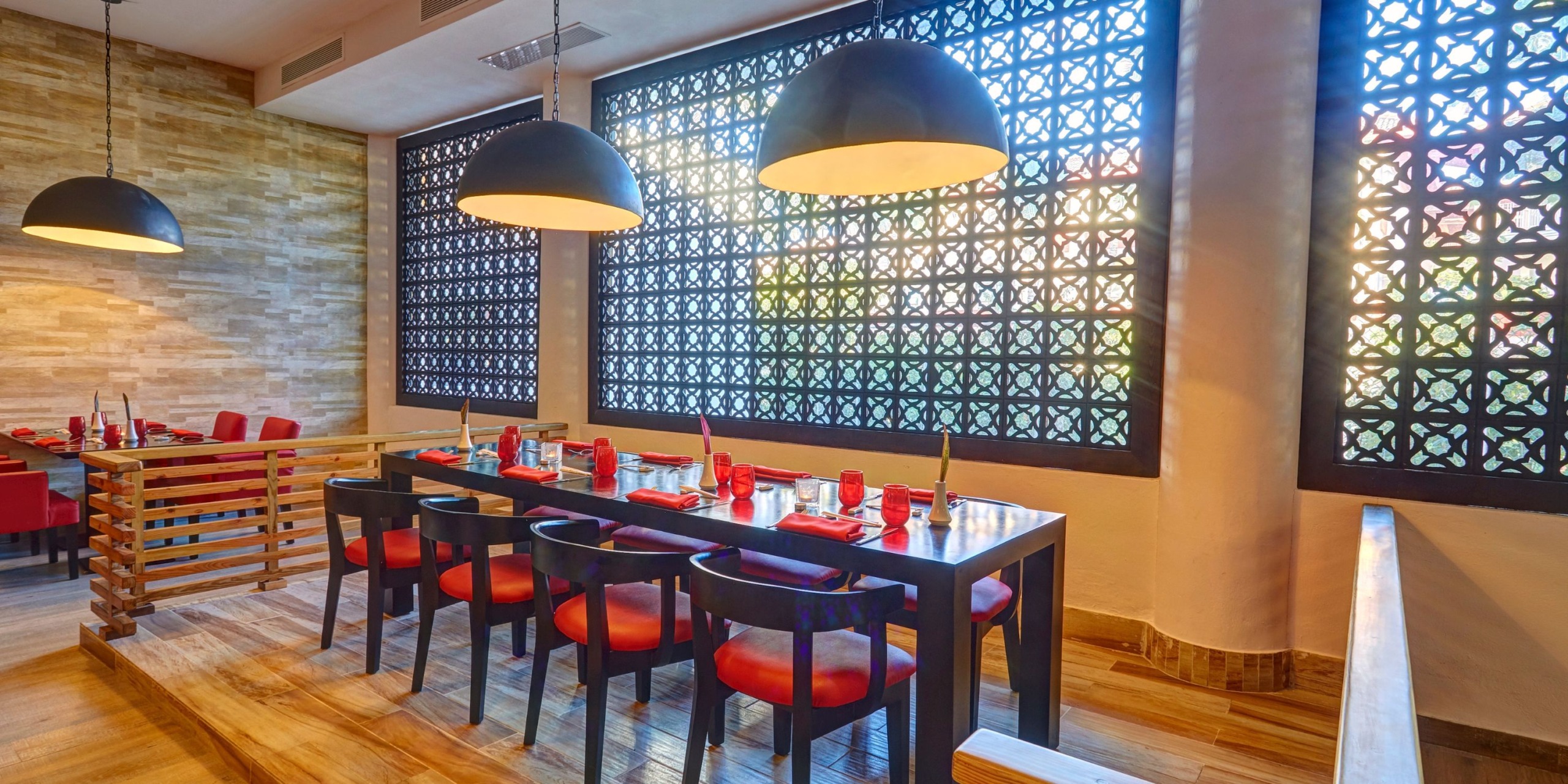 Transform your dining space into a contemporary area with the Royalton Punta Cana set, featuring a spacious table perfect for eight. It includes sleek red chairs and a trio of elegant black pendant lamps overhead, all complemented by stylish decorative lattice windows along the wall.