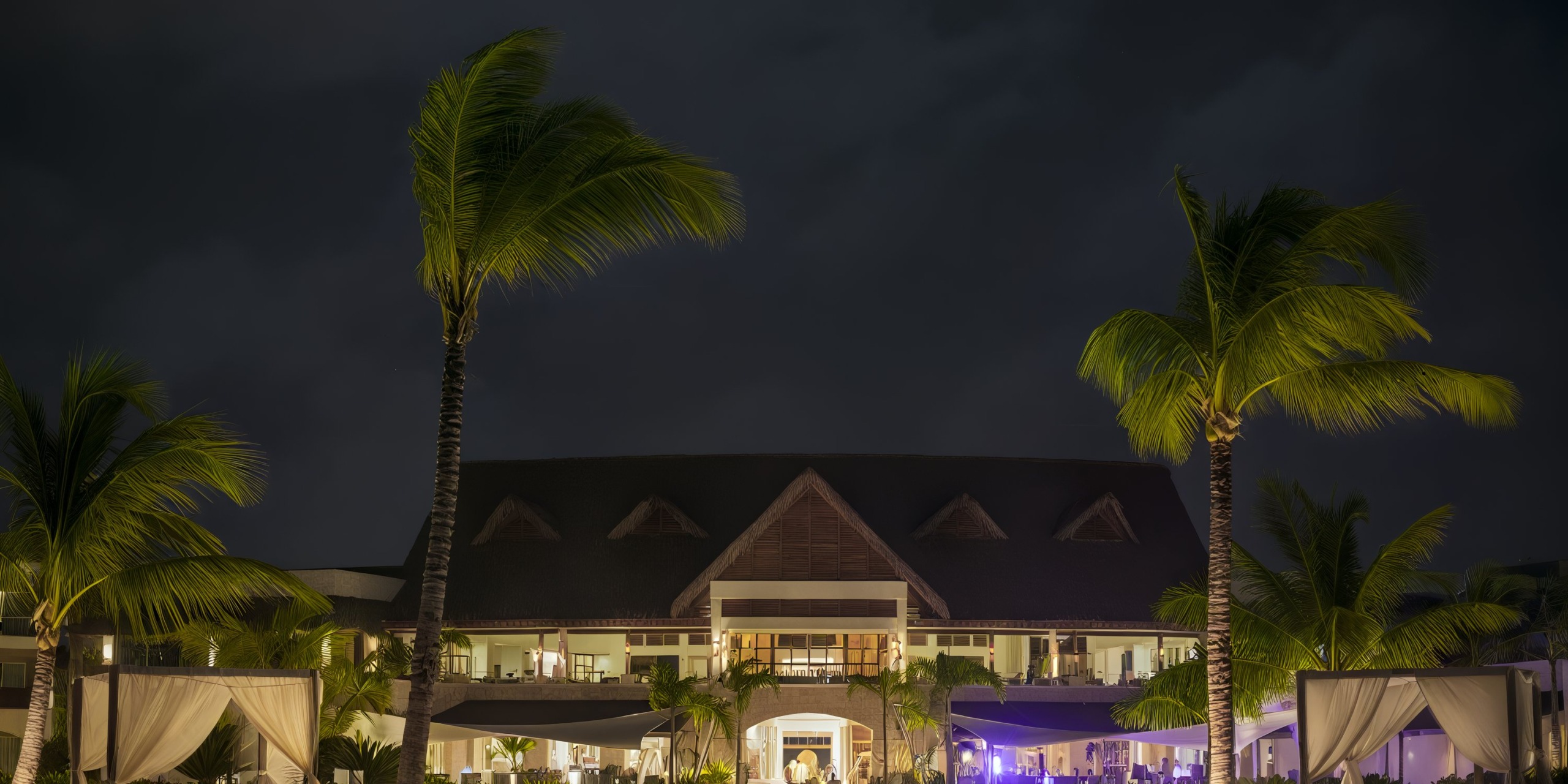 Royalton Punta Cana at night with palm trees and the illuminated main building.