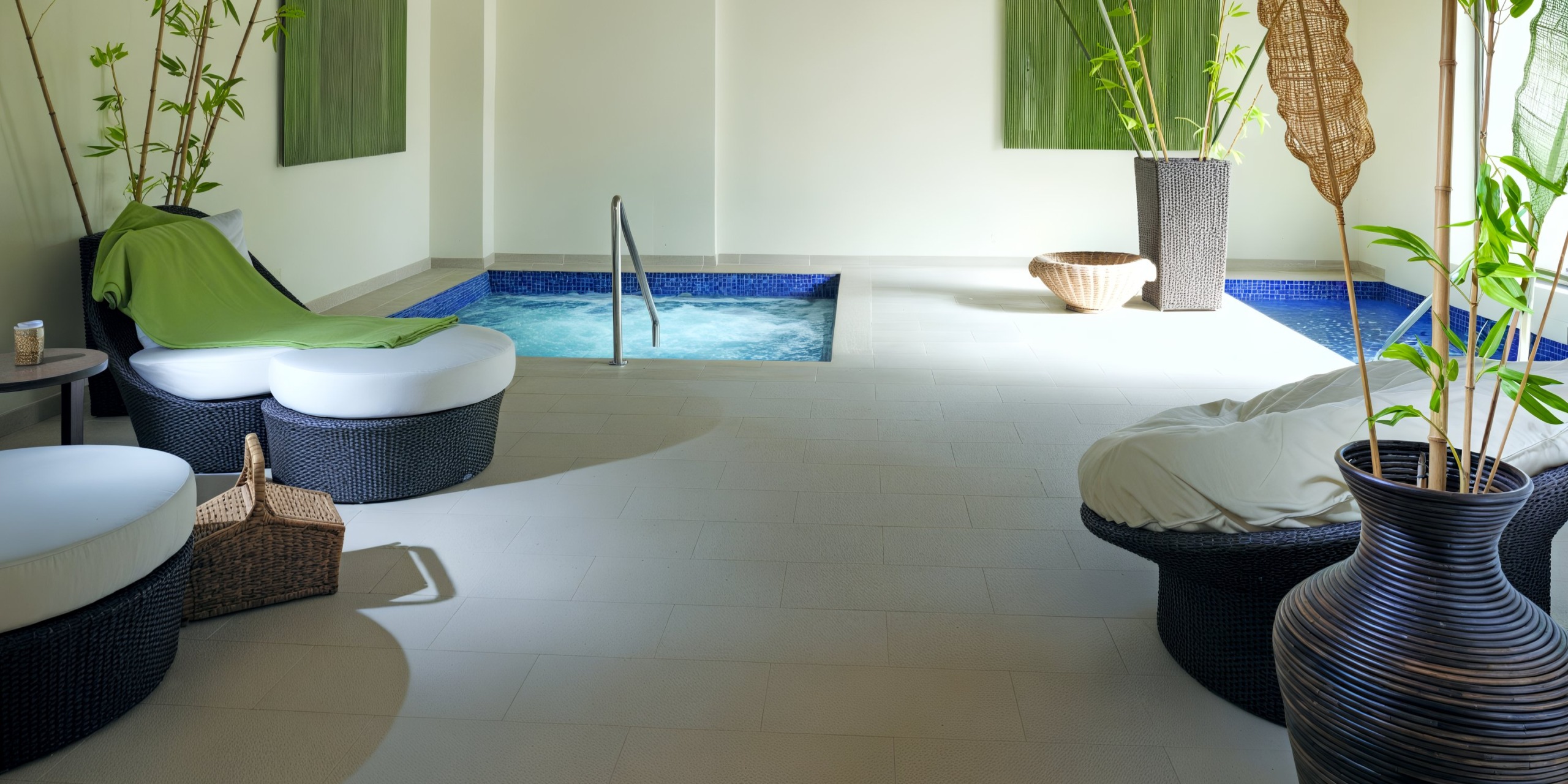 The indoor spa area at the Royalton Punta Cana features a small pool, round wicker loungers, green blankets, tall potted plants, and a wicker basket on a tiled floor.