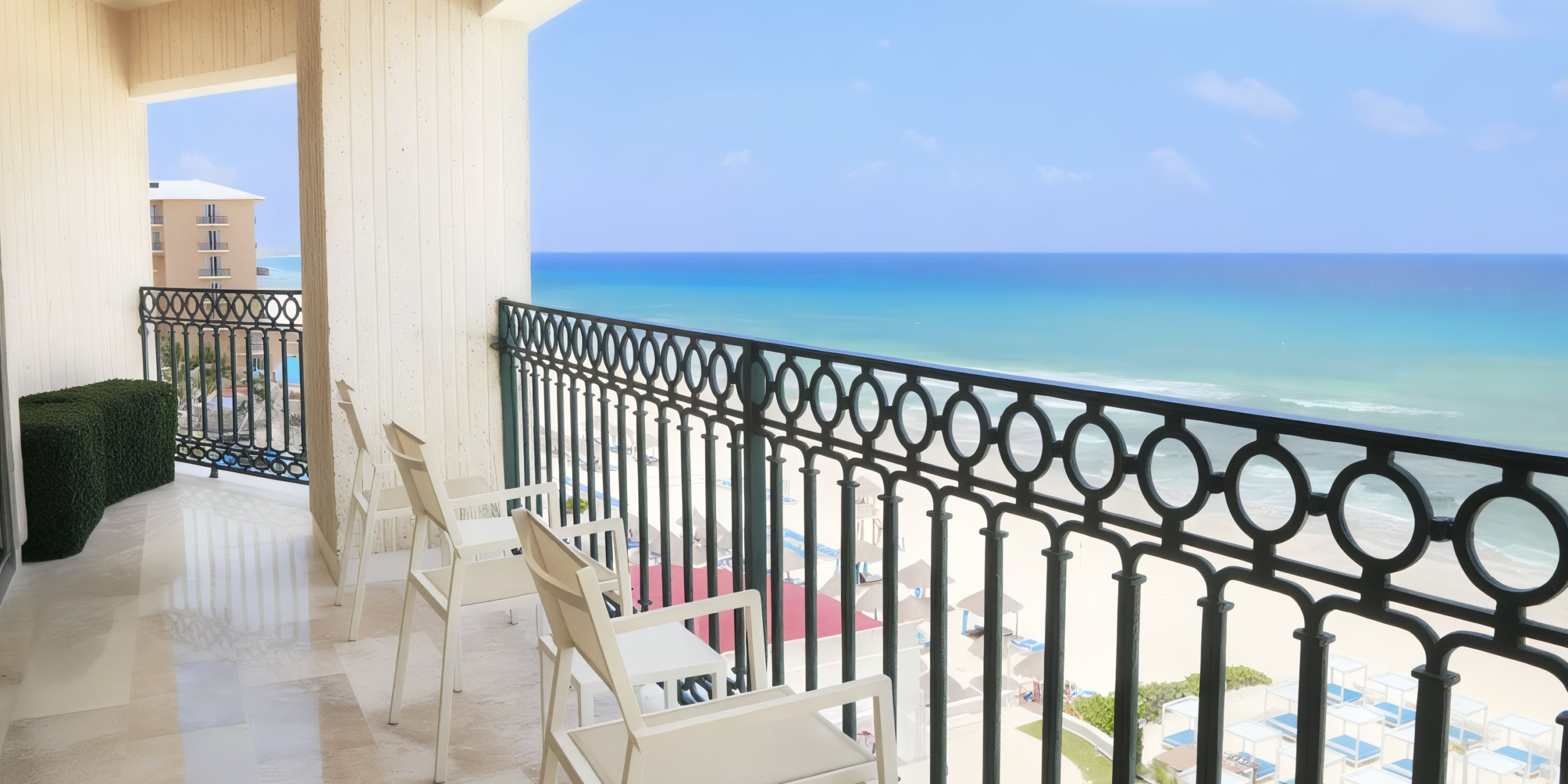 At the Sandos Cancun Lifestyle Resort, a balcony with white chairs provides a view of a sandy beach and ocean under a clear blue sky.