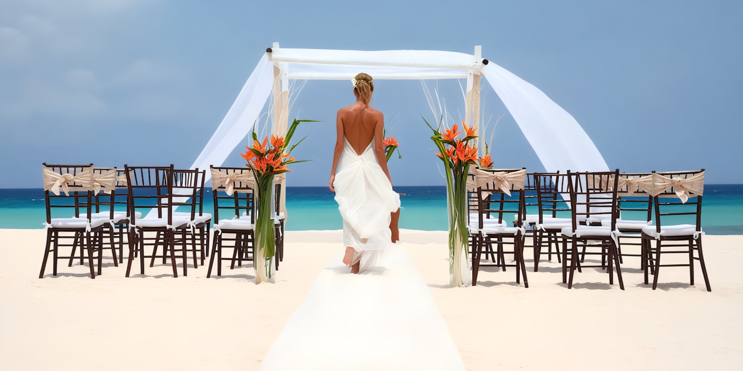A bride in a white dress walks down a sandy aisle towards a seaside wedding altar with chairs on either side, set against the backdrop of the blue ocean at Sandos Cancun Lifestyle Resort.