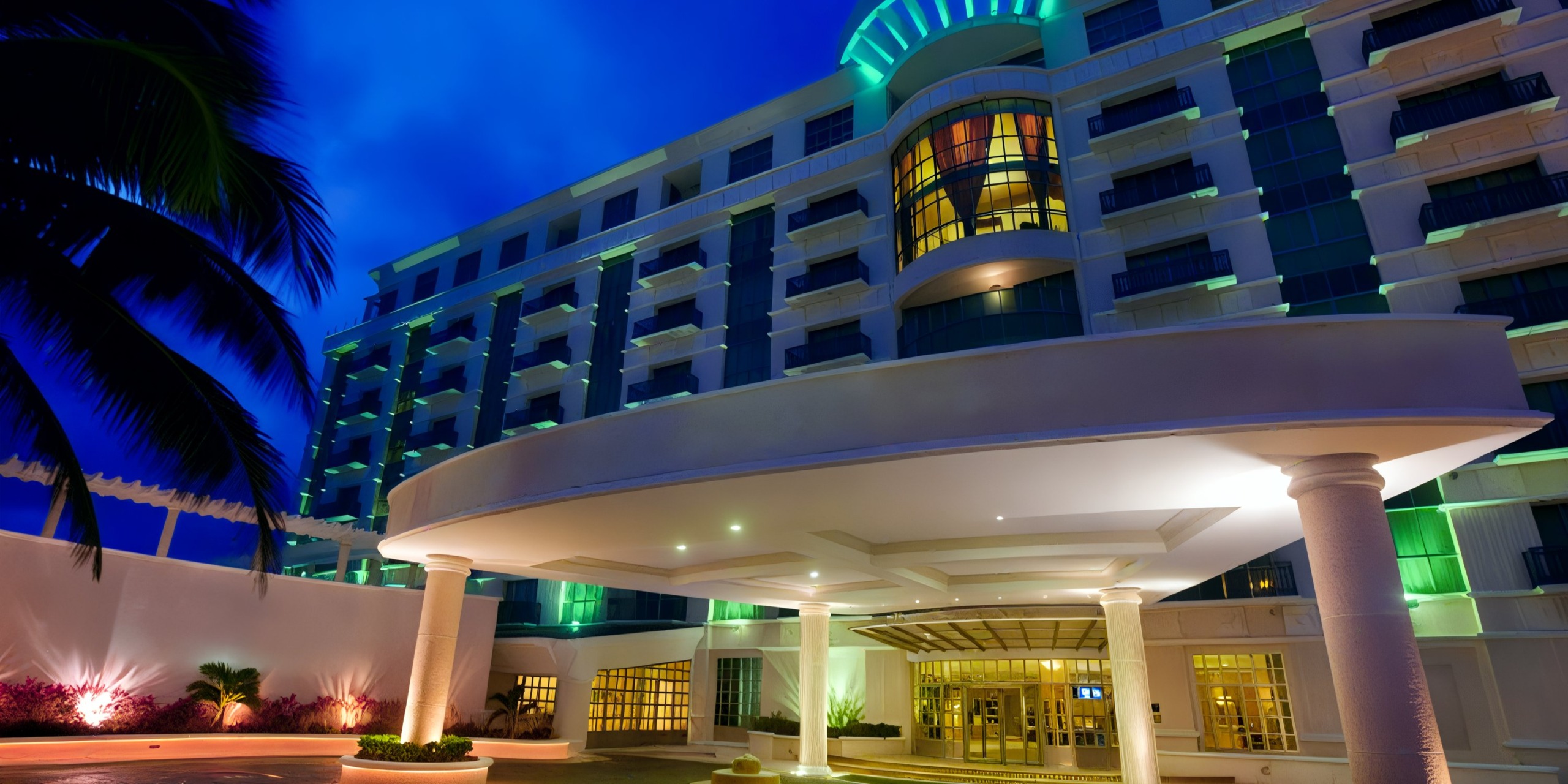 Night view of the brightly lit entrance to Sandos Cancun Lifestyle Resort, featuring a circular driveway.