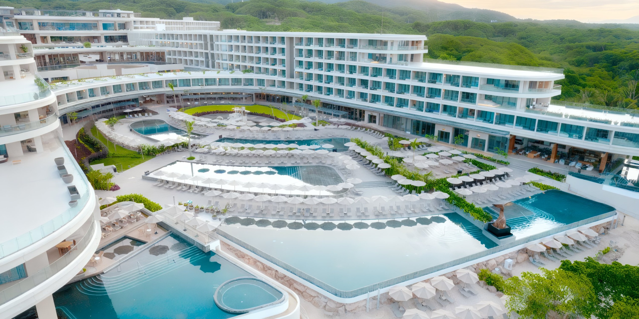 Aerial view of Secrets Bahia Mita, a large, modern resort surrounded by lush greenery, featuring multiple swimming pools, sun loungers, and a curving architectural design.
