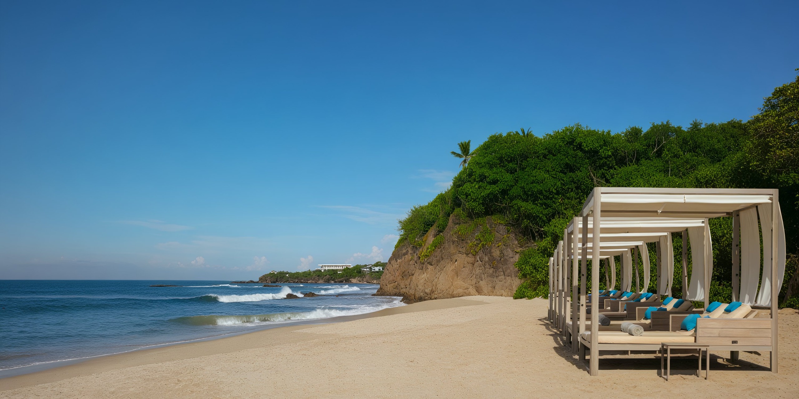 Experience the serene beauty of Secrets Bahia Mita, where you can relax on lounge chairs under canopies set on sandy stretches, surrounded by lush greenery and a rocky cliff. Enjoy the soothing ocean waves gently crashing under a clear blue sky.
