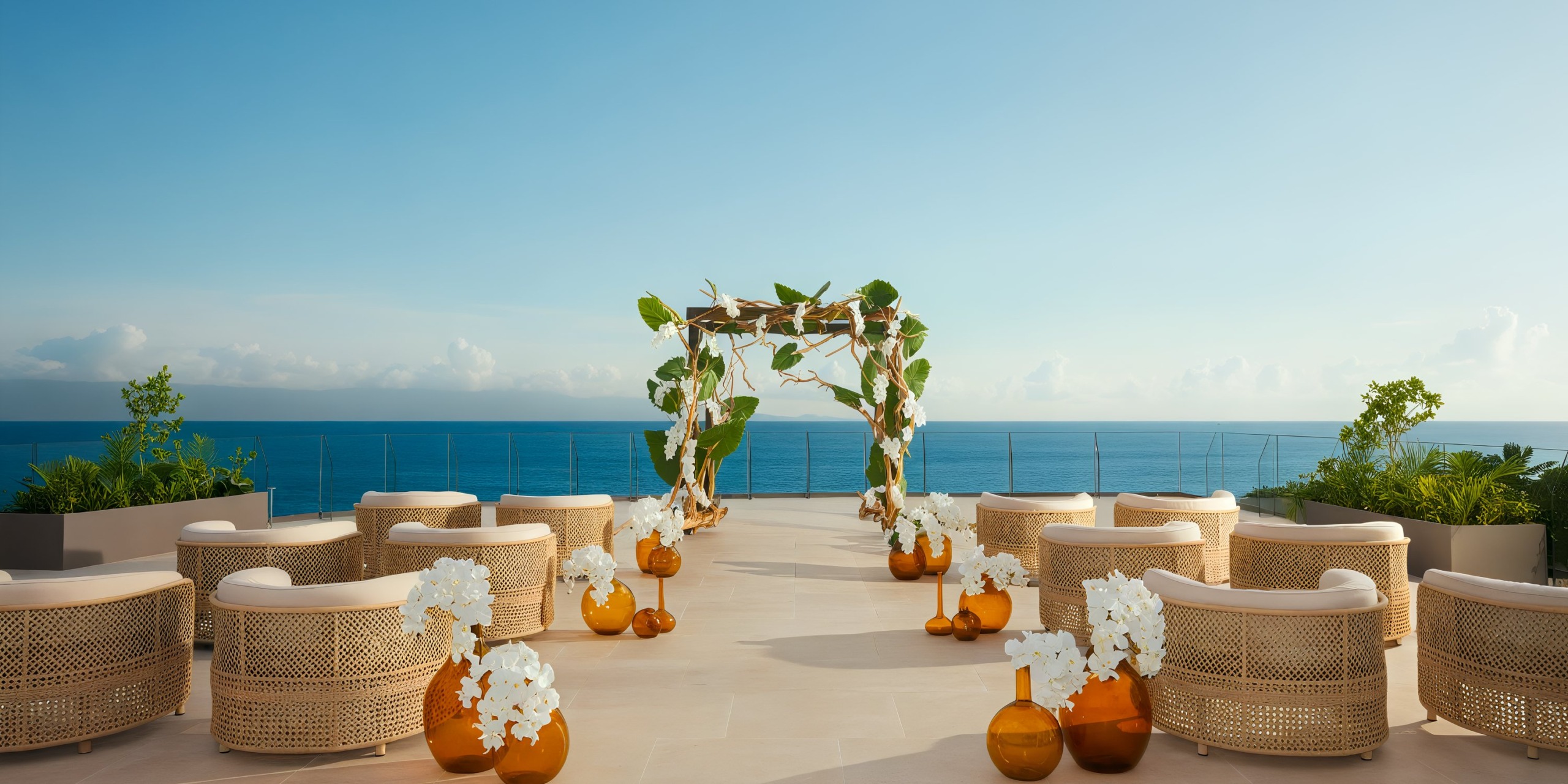 The Secrets Bahia Mita outdoor wedding setup features wicker chairs neatly arranged in rows, a stunning floral arch, and a breathtaking ocean view backdrop. White flowers in amber vases are elegantly placed beside the chairs.