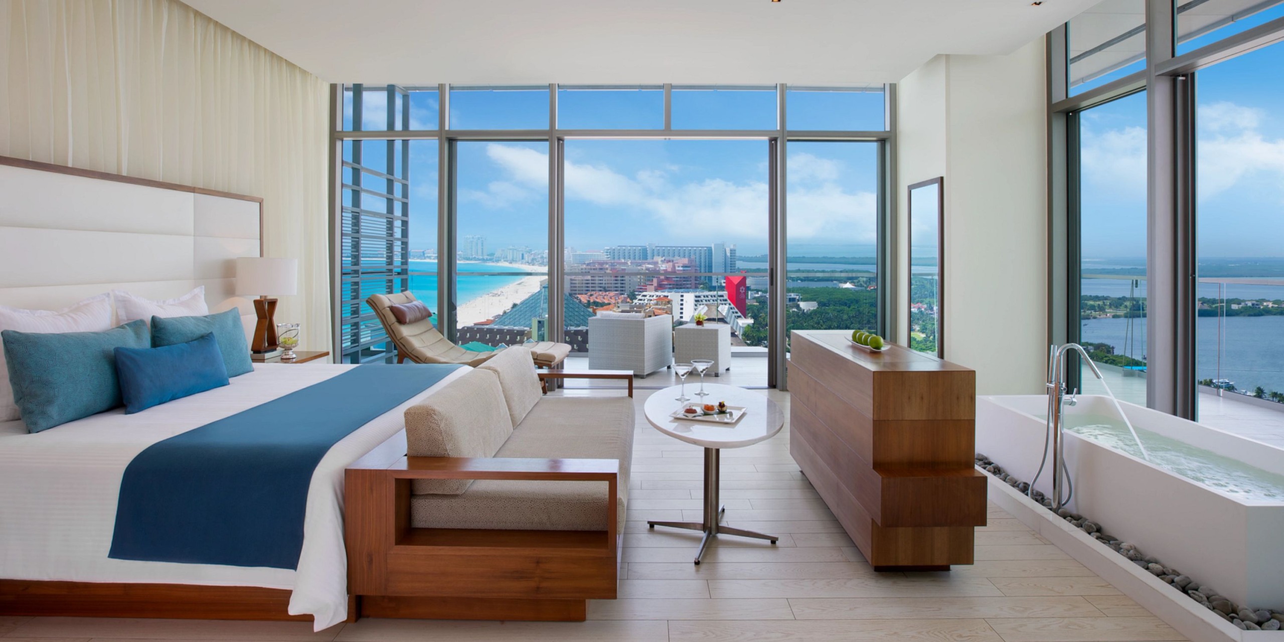 Experience the Secrets the Vine Cancun with a spacious room that includes a large bed, cozy seating area, and a bathtub. Enjoy stunning views of a beach, sea, and distant buildings through the floor-to-ceiling windows.