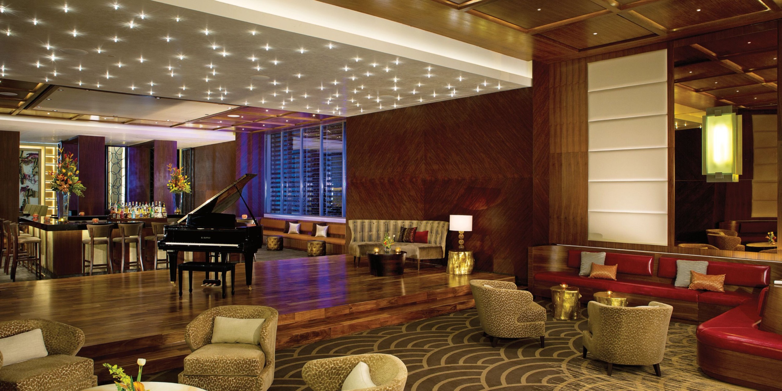 Experience the luxury of Secrets the Vine Cancun's hotel lounge, featuring a grand piano, modern seating arrangements, and ambient lighting. The space is adorned with elegant decor incorporating wooden accents and includes a chic bar area for guests to enjoy.