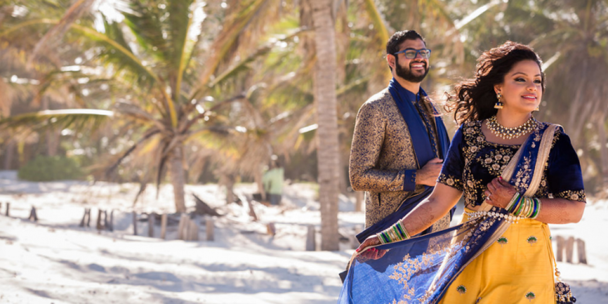 Shruti and Nikhil pose together on the beach amongst palm trees