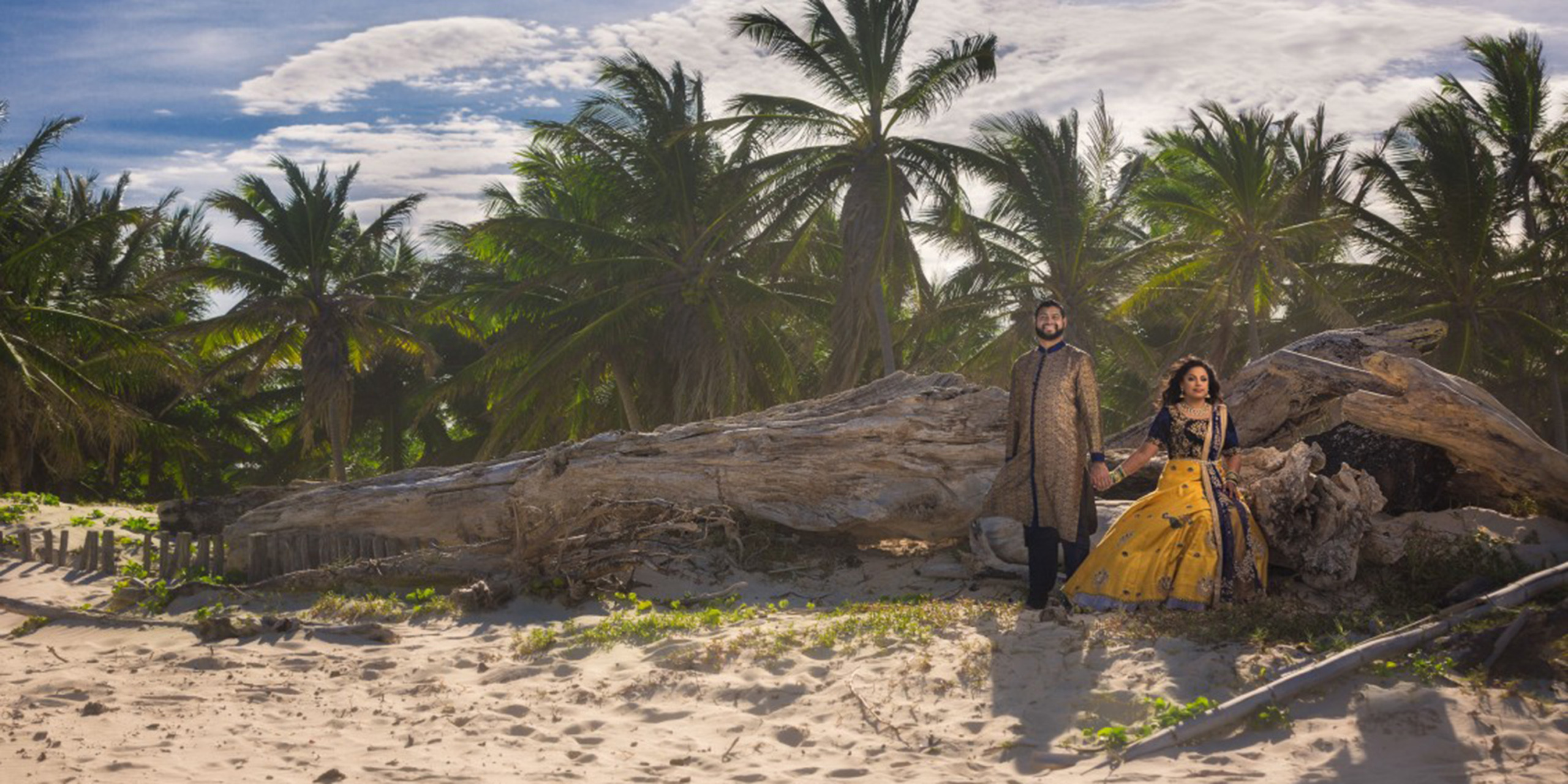 Shruti and Nikhil pose together on the beach amongst palm trees